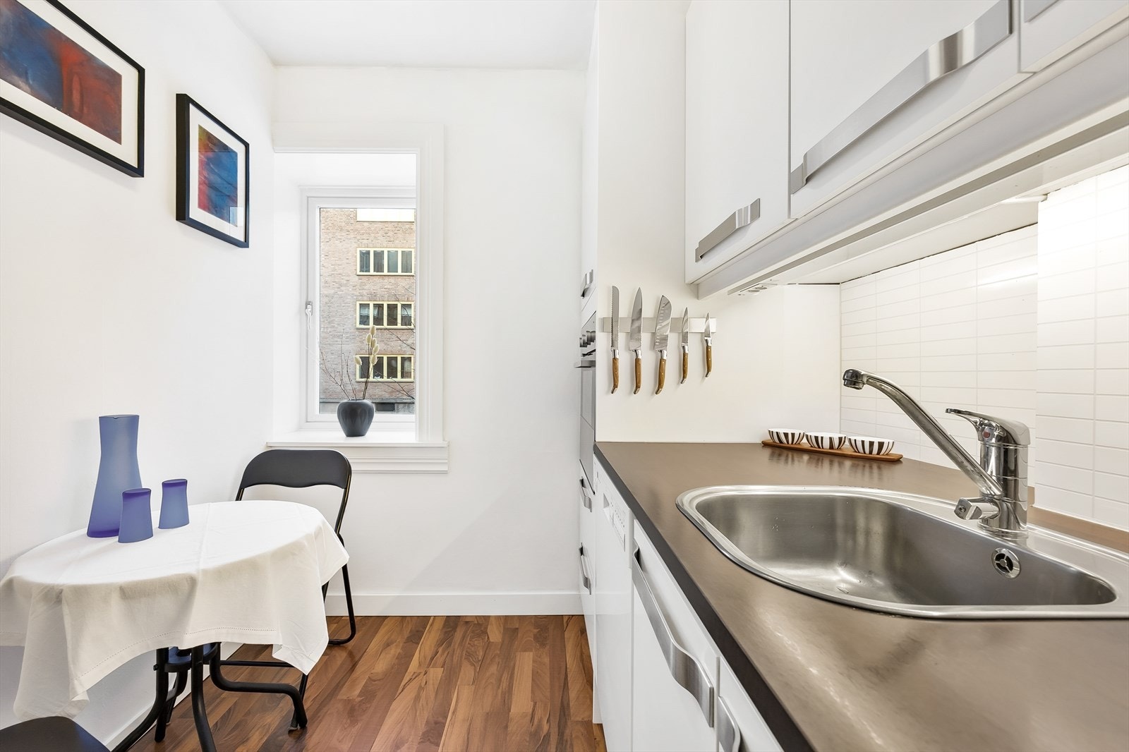 Kjøkkeninnredningen består av hvite glatte fronter i både over- og underskap, belysning, og laminat benkeplate med oppvaskkum Galleribilde