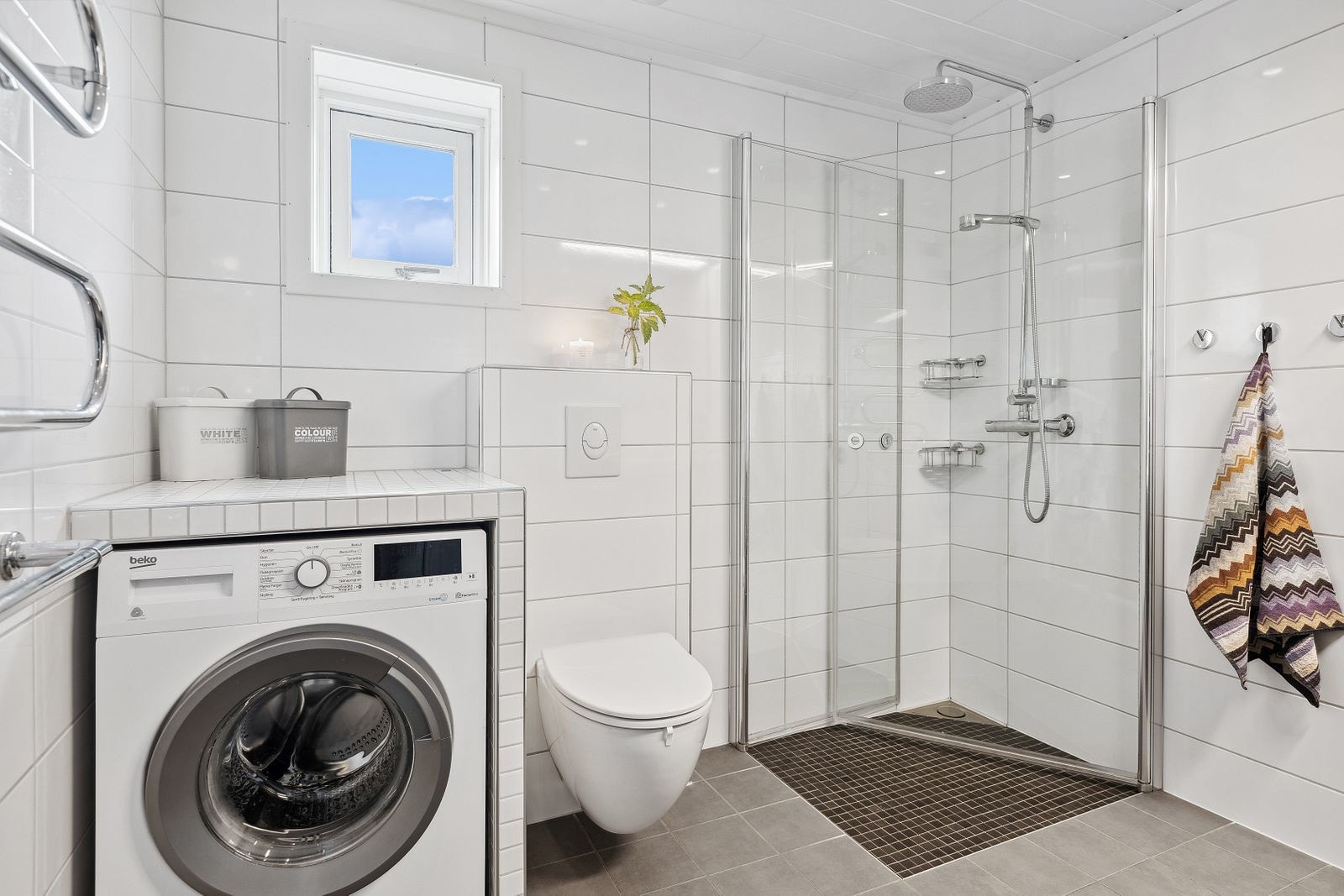 Badet inneholder vegghengt servantskap med heldekkende servant, dusjhjørne, vegghengt toalett og har opplegg for vaskemaskin. Galleribilde