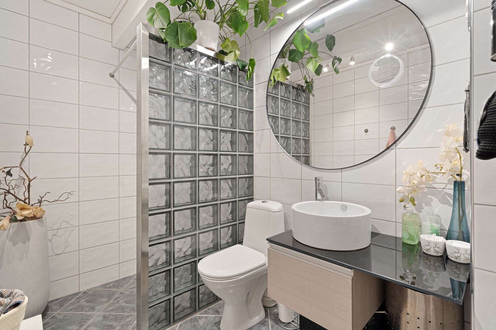 Badet har fliser på gulv og vegger, dusjnisje bak vegg i glassbyggerstein, gulvvarme og spotlights. Galleribilde