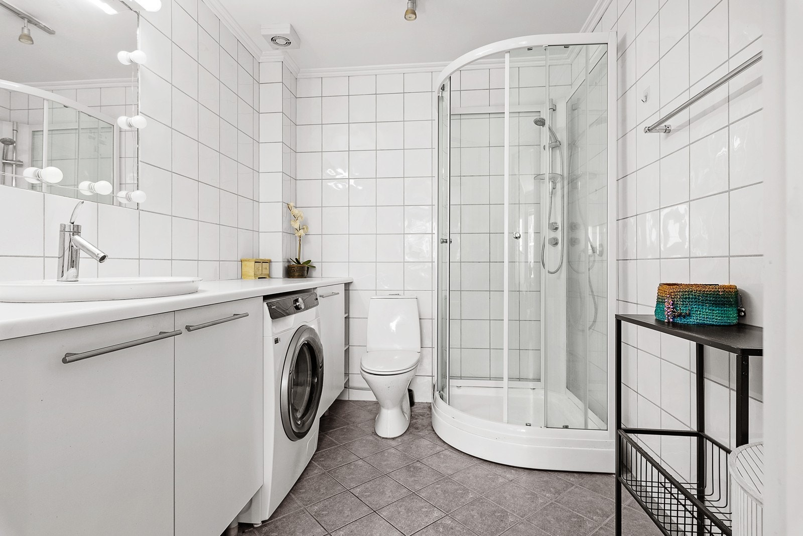 Flislagt bad med varmekabler. Badet inneholder servant m/skap, dusjkabinett, wc og opplegg for vaskemaskin. Galleribilde