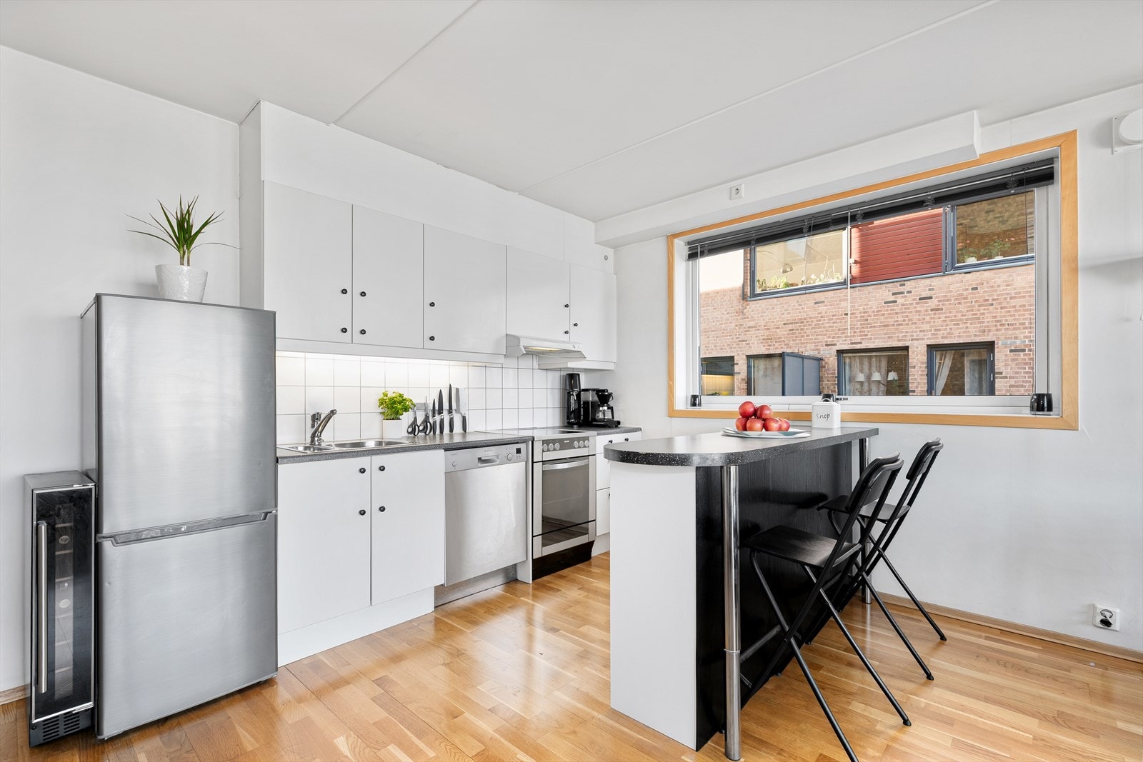 Pent kjøkken med mye skap- og benkeplass. Kjøkkeninnredning med hvite glatte fronter, laminat benkeplate med nedfelt kum i stål og fliser over kjøkkenbenken. Galleribilde