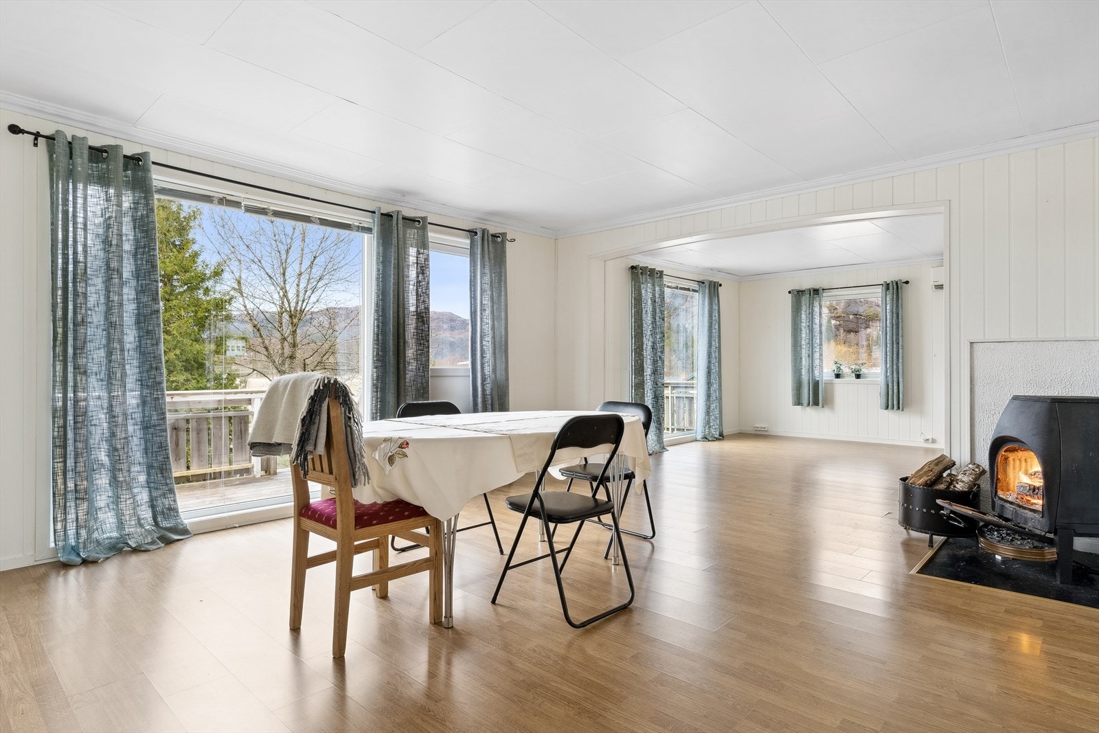 Stor og romslig stue med store vindusflater, vedovn og dør ut til terrasse. Galleribilde