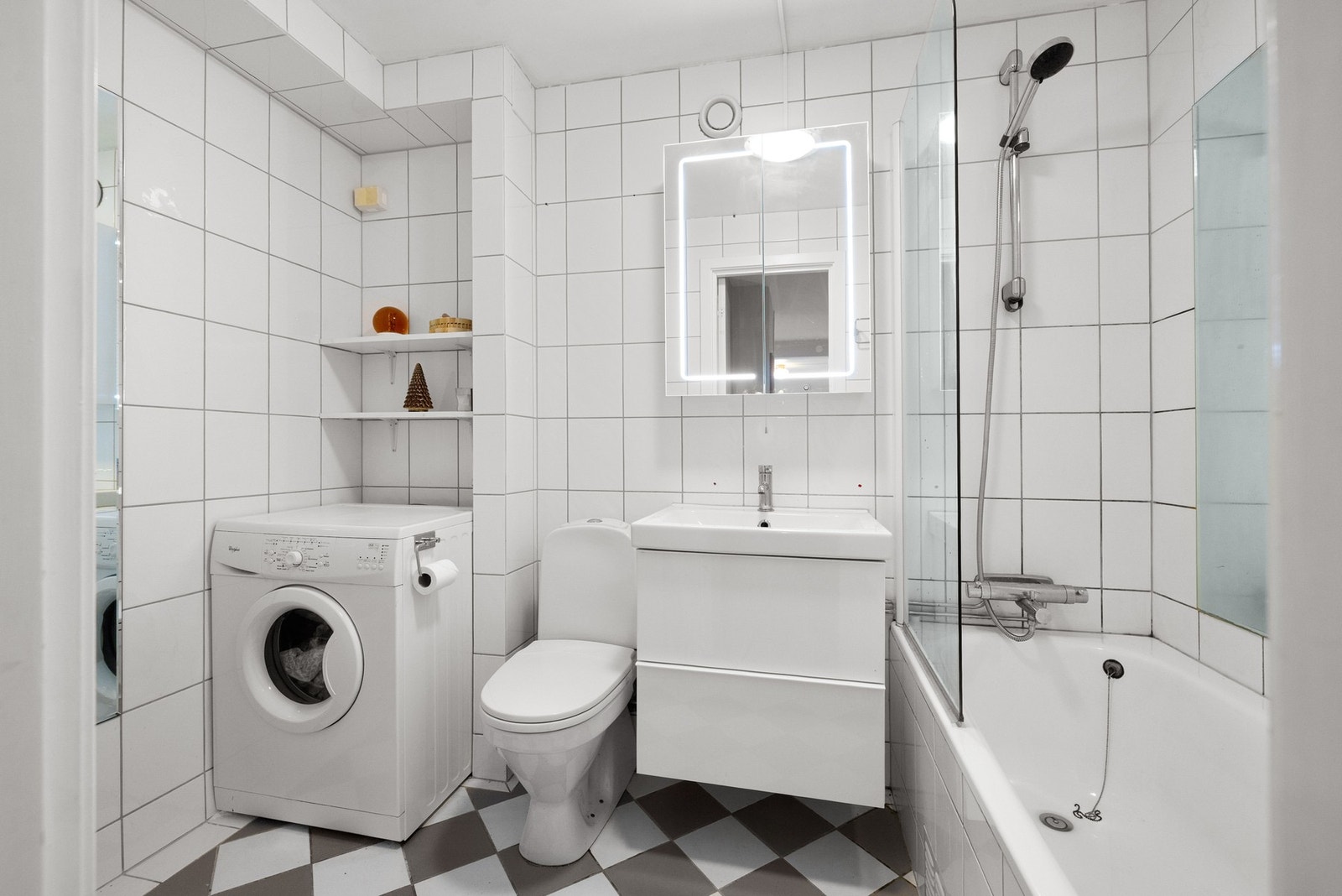 Badet er lyst og tiltalende, med praktisk opplegg for vaskemaskin i en nisje med hyller. Det finnes også strømuttak for en eventuell tørketrommel. Galleribilde