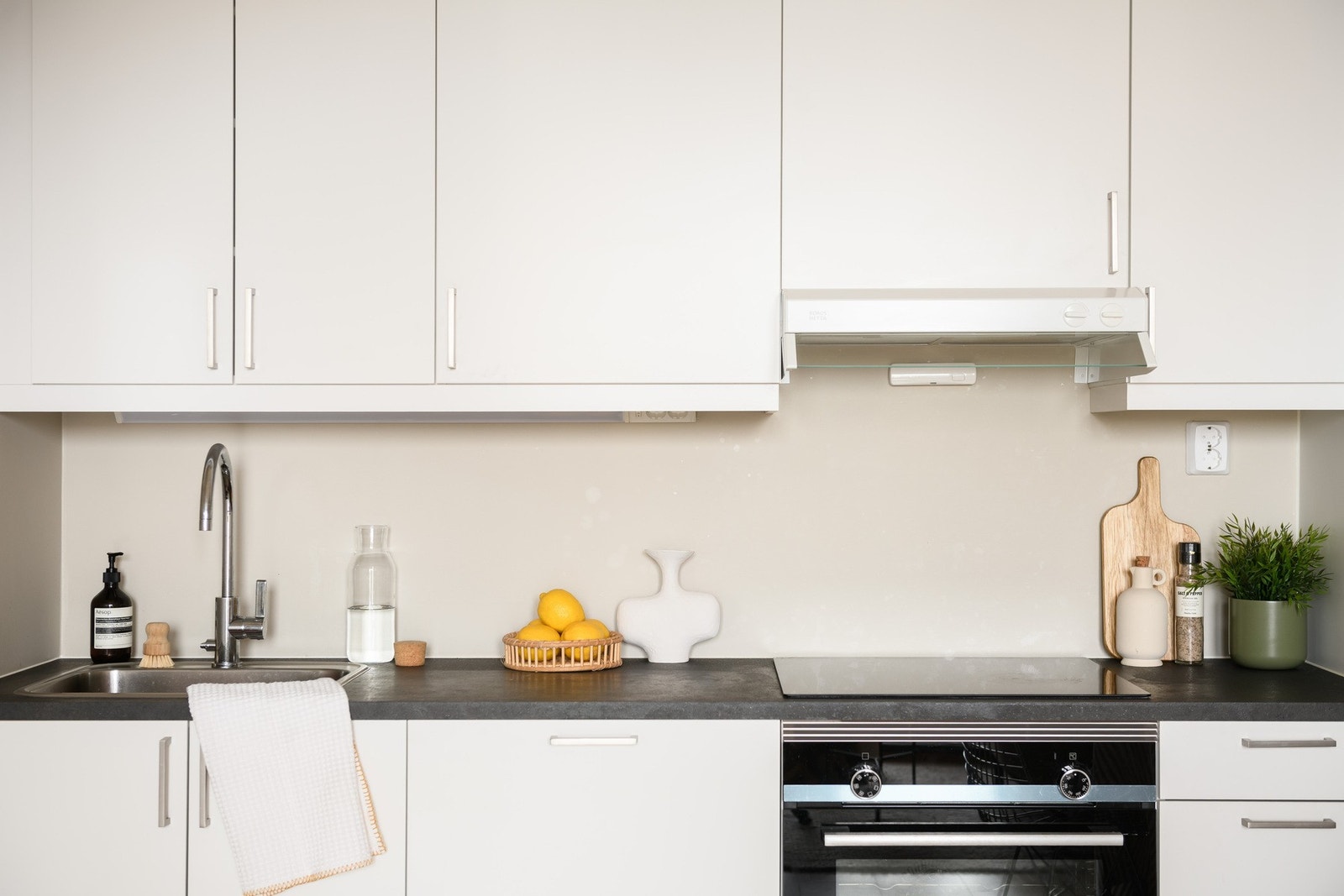 Innredningen er kompakt med høye overskap, hvite, glatte fronter og benkeplate i grå laminat. Galleribilde