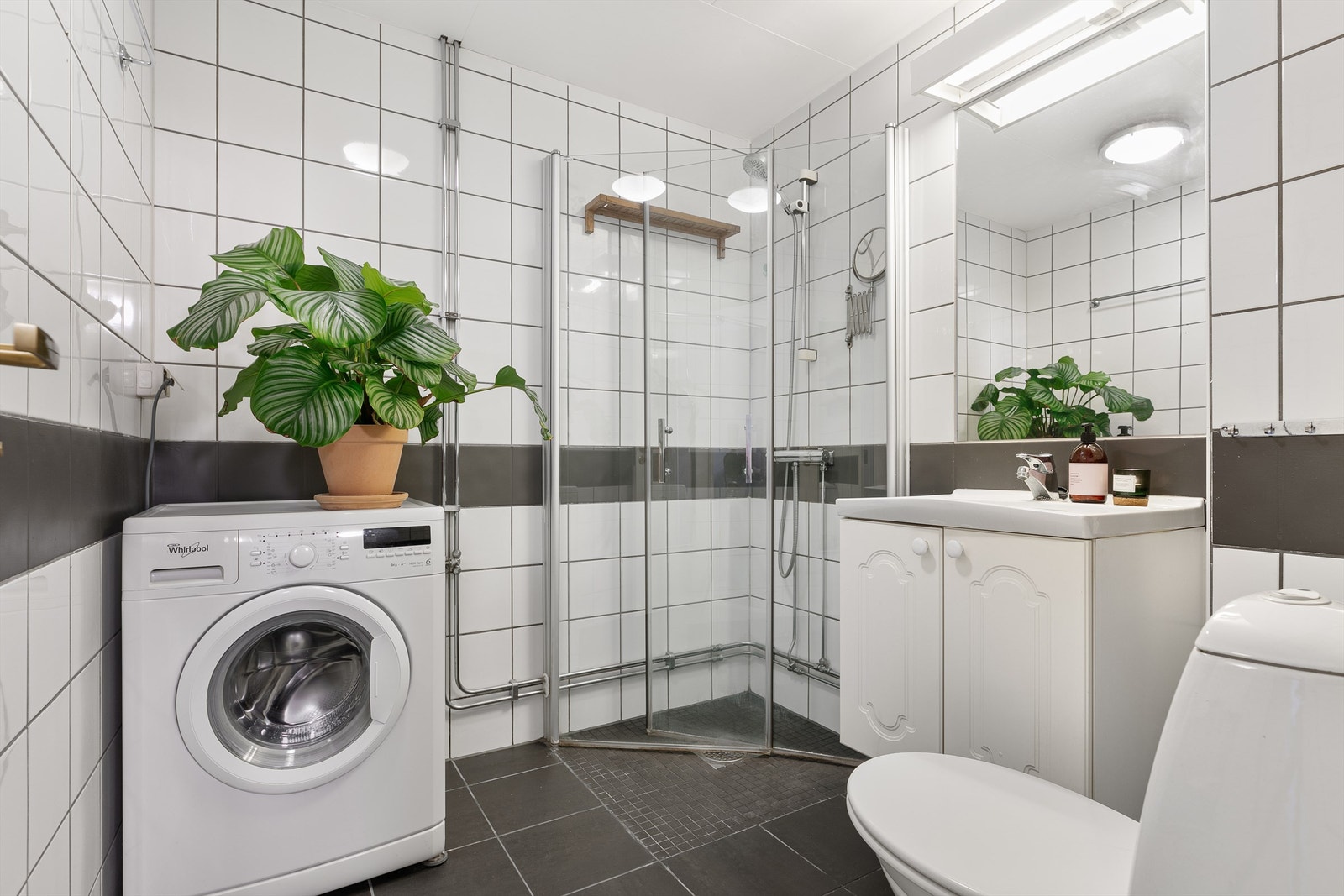Badet har mørkegrå gulvfliser med varme, i fin kontrast til hvite veggfliser med innslag av den samme grånyansen. Galleribilde