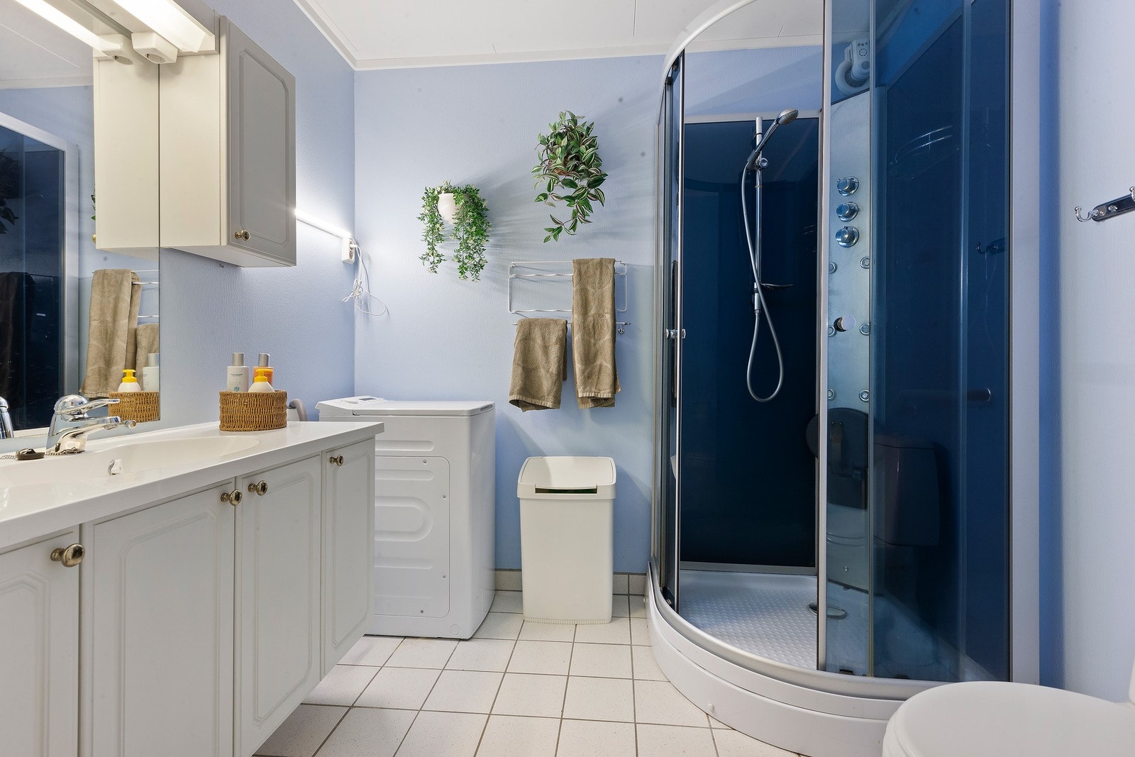 Badet har en lys innredning og flislagt gulv med vannbåren varme. Det er dusjkabinett og opplegg for vaskemaskin. Galleribilde