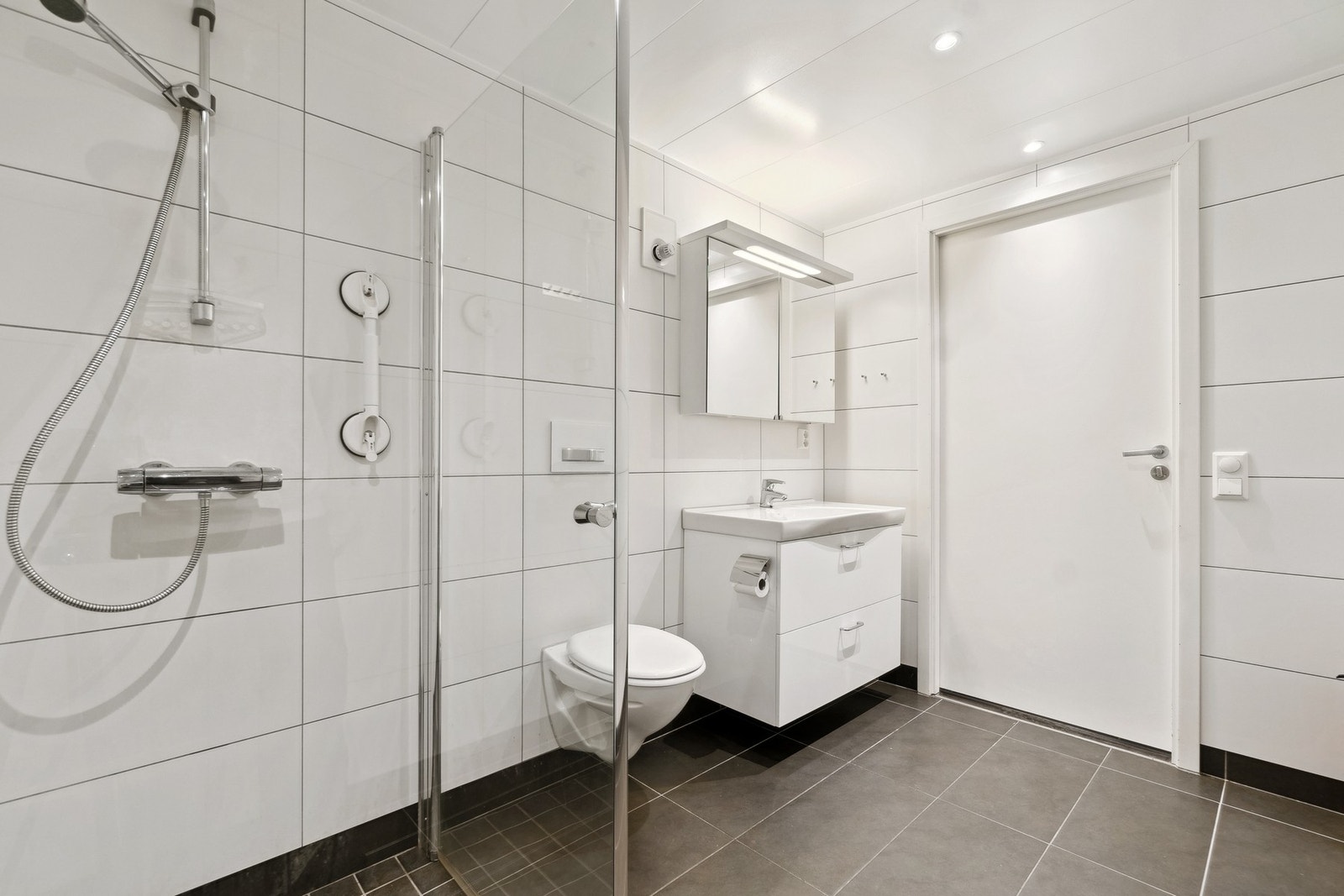 Badet er utstyrt med vegghengt toalett, dusjarmatur og innfellbare dusjdører, servant med underskap og opplegg for vaskemaskin. Galleribilde