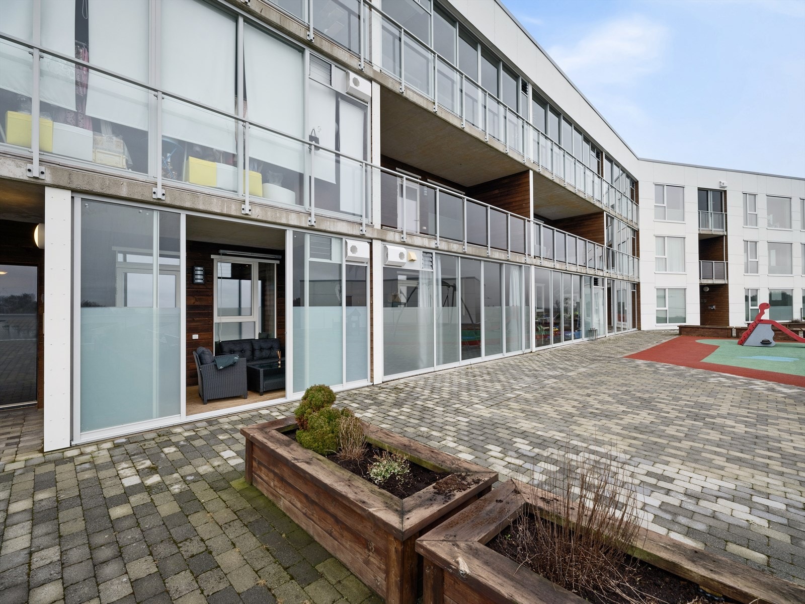 Moderne leilighetskompleks med store vinduer og romslig balkong. Flott felles uteområde med lekeplass og plantekasser. Galleribilde