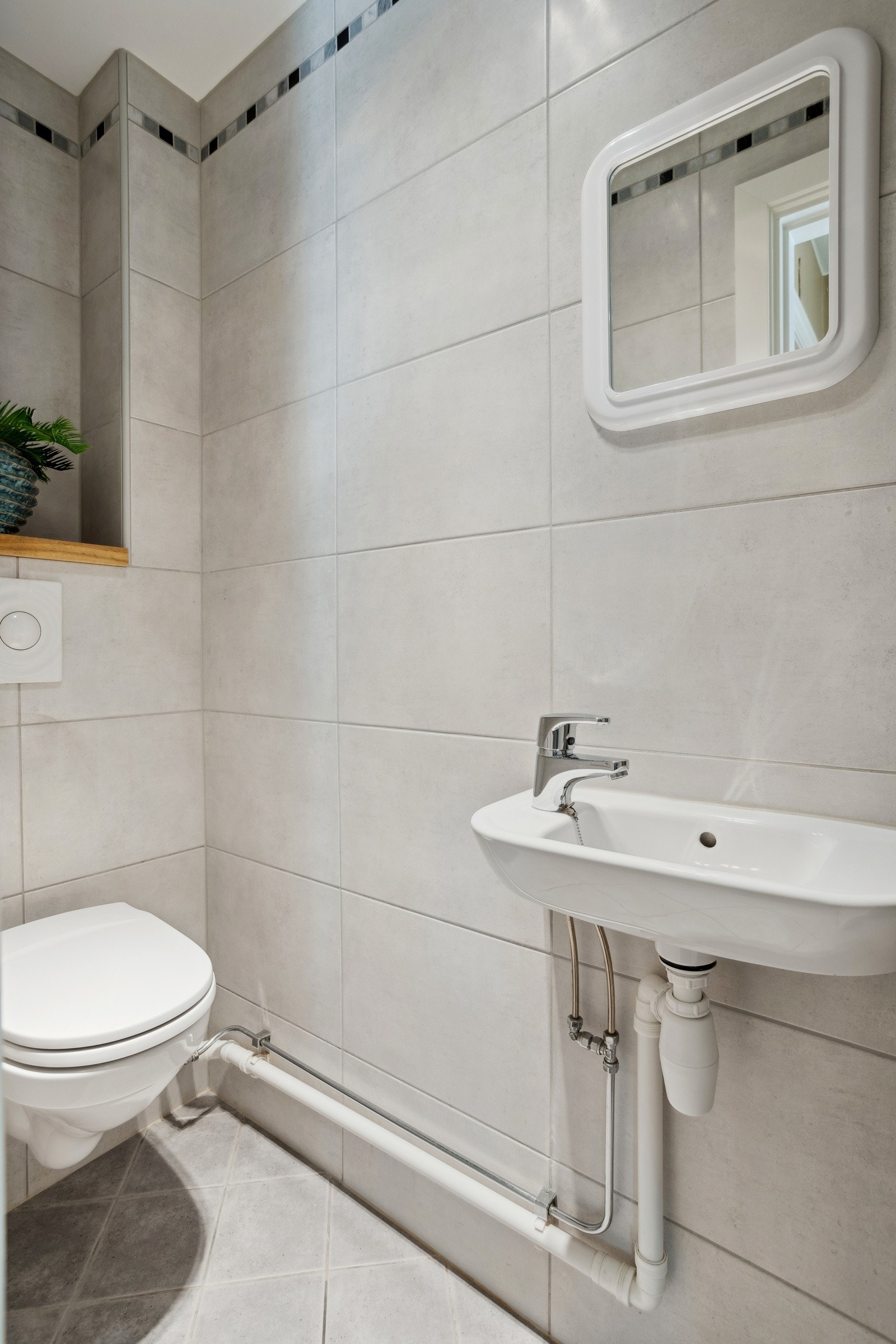 Pent flislagt toalettrom med enkel servant og vegghengt klosett. Galleribilde