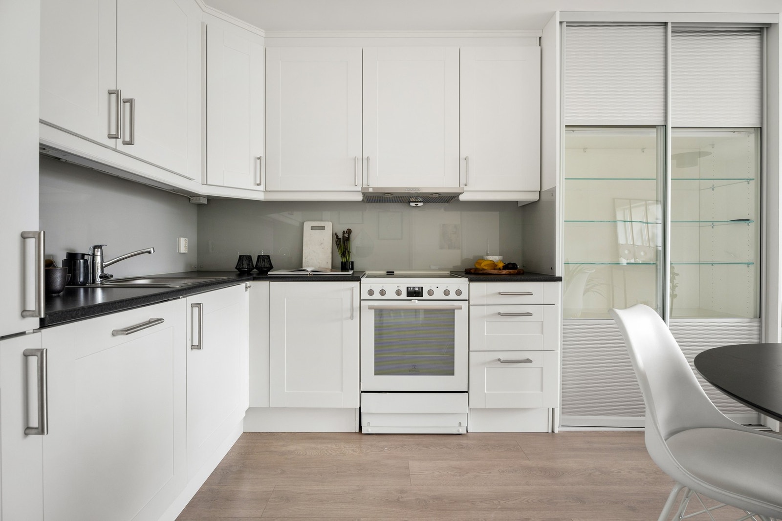 Innredningen har takoppforede skap, hvite rammefronter i klassisk stil og benkeplate i mørk laminat med nedfelt vaskekum. Galleribilde