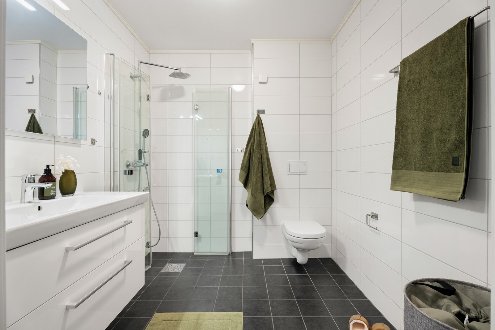 Badet har grå fliser på gulv med gulvvarme, hvite fliser på veggene og glatt, hvitmalt himling. Galleribilde