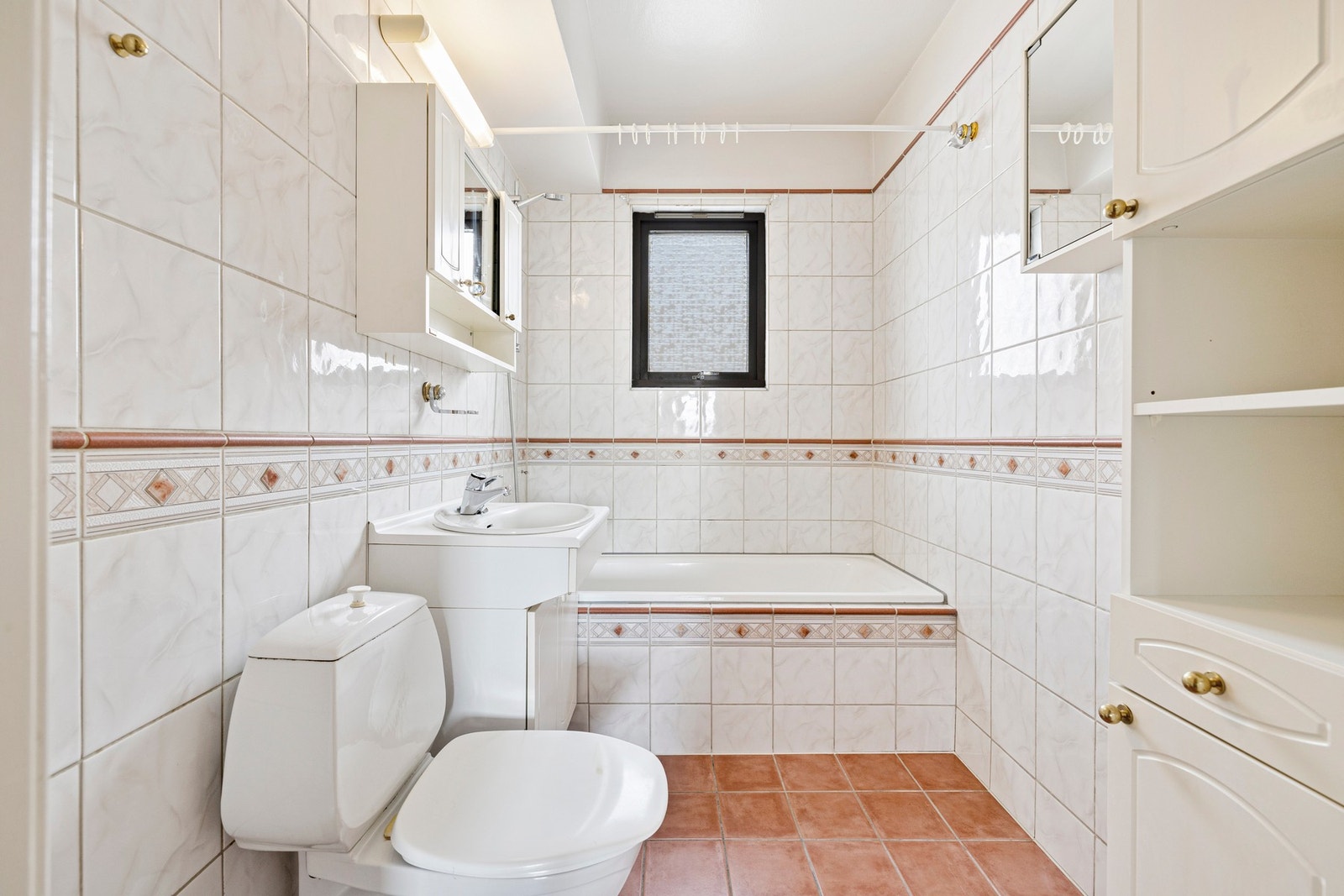 Eldre flislagt baderom fra ukjent årstall med servant, toalett og innebygget badekar. Galleribilde