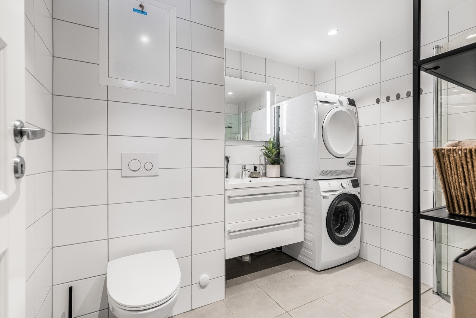 Badet har et delikat uttrykk med hvite veggfliser og lysegrå fliser på gulvet. Downlights og varmekabler er montert. Galleribilde