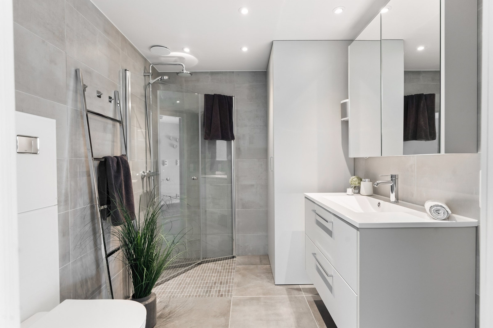 Stort hovedbad med lekre tidsriktige flisvalg, innfellbare dusjvegger og praktisk skap for vaskemaskin og tørketrommel Galleribilde