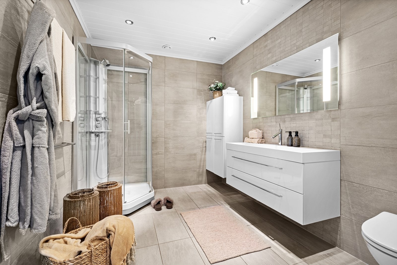 Badet er helfliset med italienske steinfliser med tilhørende italienske moasikkfliser fra 2009, utført av fagfolk. Det inneholder et praktisk dusjkabinett, vegghengt toalett, samt baderomsinnredning med speil over. Det er downlights i himling. Galleribilde