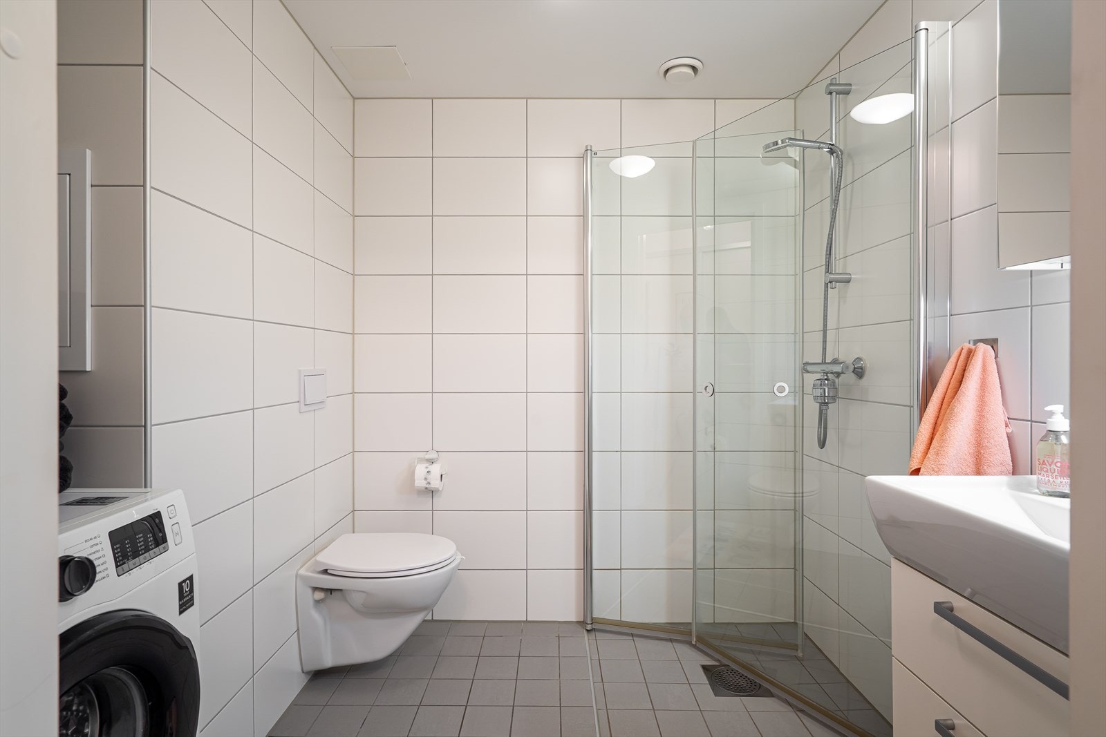 Her finner du vegghengt toalett, dusjhjørne med innfellbare dører i herdet glass og servant med speilskap og belysning. Galleribilde