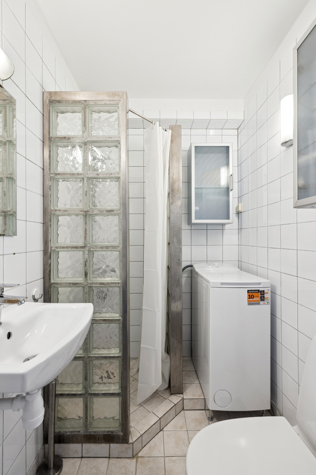 Flislagt bad med dusj, glassbyggersten og vaskemaskin. Galleribilde