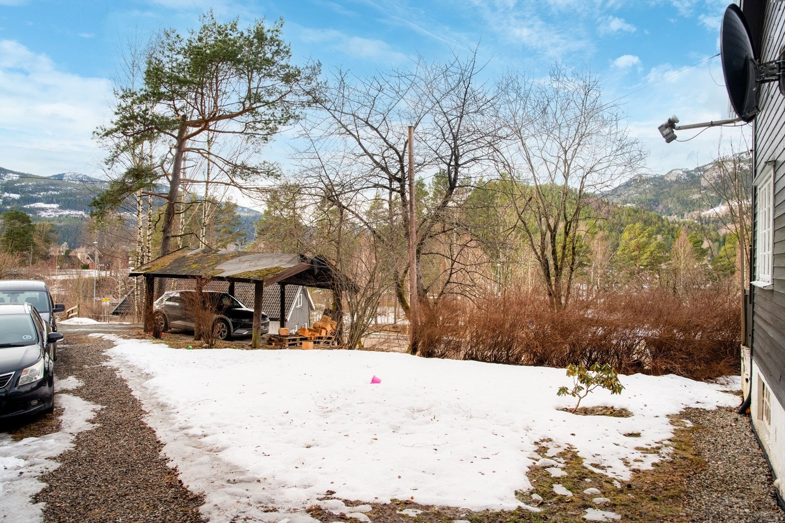 Det er godt med parkeringsplasser på gruset gårdsplass, samt i carporten. Denne opplyses å være i dårlig forfatning. Galleribilde