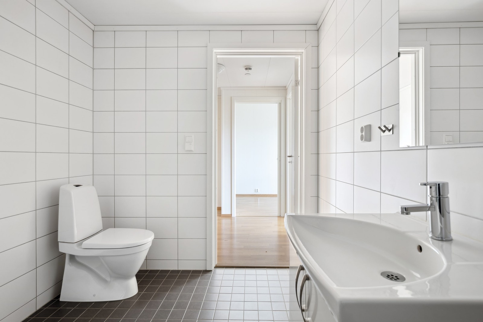 Badet har flislagt gulv med varmekabler, flislagte vegger og en himling med malt overflate. Innredning med vegghengt servantskap med heldekkende servant og speil. Galleribilde