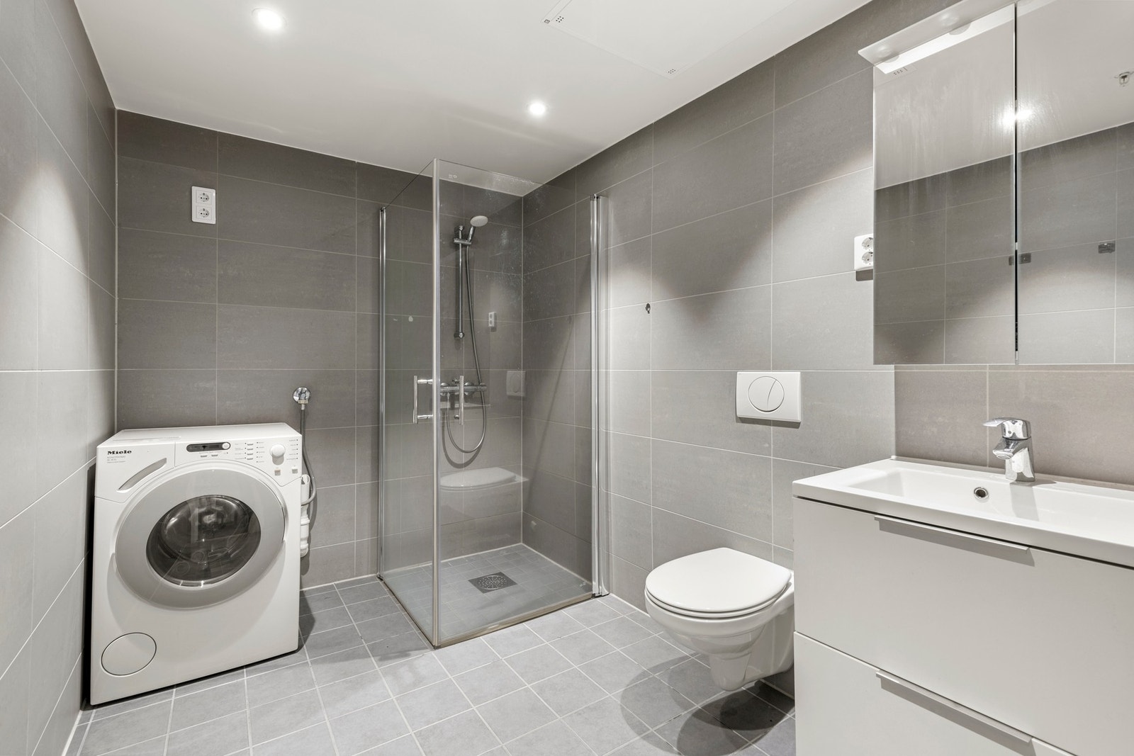 Stilrent baderom med store fliser og integrert belysning. God plass til vaskemaskin, og dusjhjørnet gir en eksklusiv følelse. Galleribilde