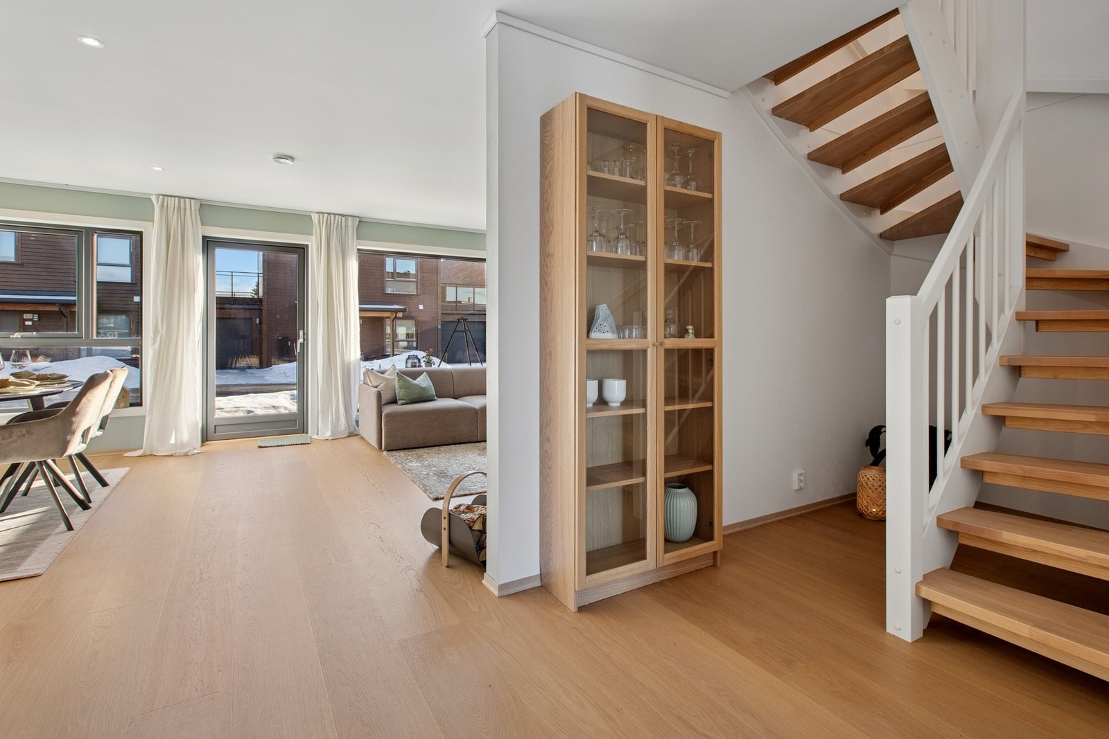 Den åpne løsningen mellom stue og kjøkken gir en luftig og innbydende atmosfære. Store vindusflater slipper inn rikelig med dagslys, mens den åpne trappen bidrar til en naturlig flyt mellom etasjene. Galleribilde