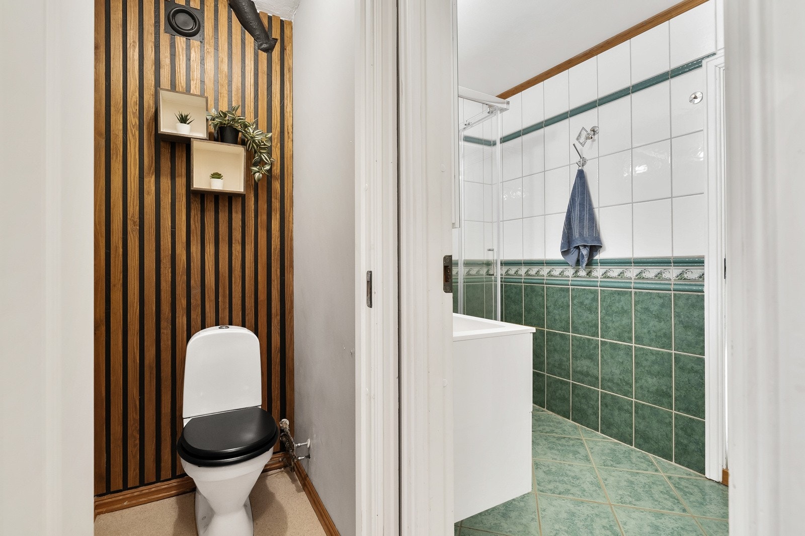 Toalettrommet har gulvbelegg, lysmalte vegger, en fondvegg med moderne spilepanel, samt et gulvmontert toalett. Galleribilde