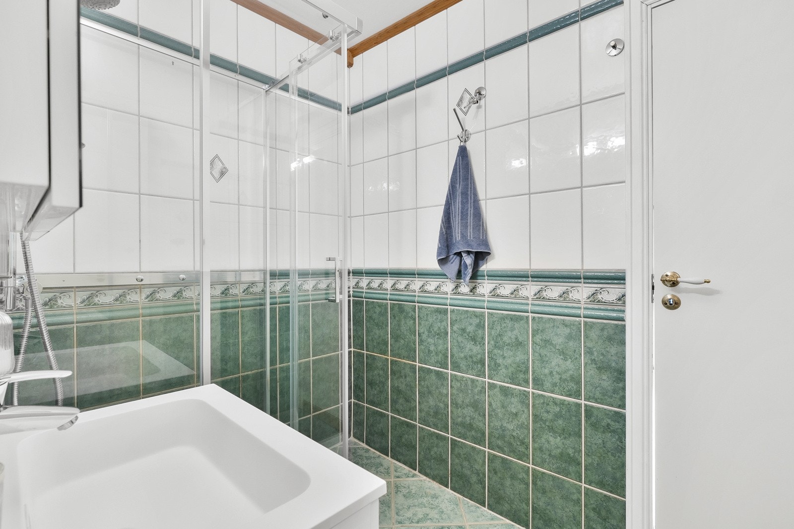 DSC02812Badet har grønne fliser på gulvet og til brystningshøyde på veggen, hvite veggfliser ellers og hvitmalt himling med brune lister. Galleribilde