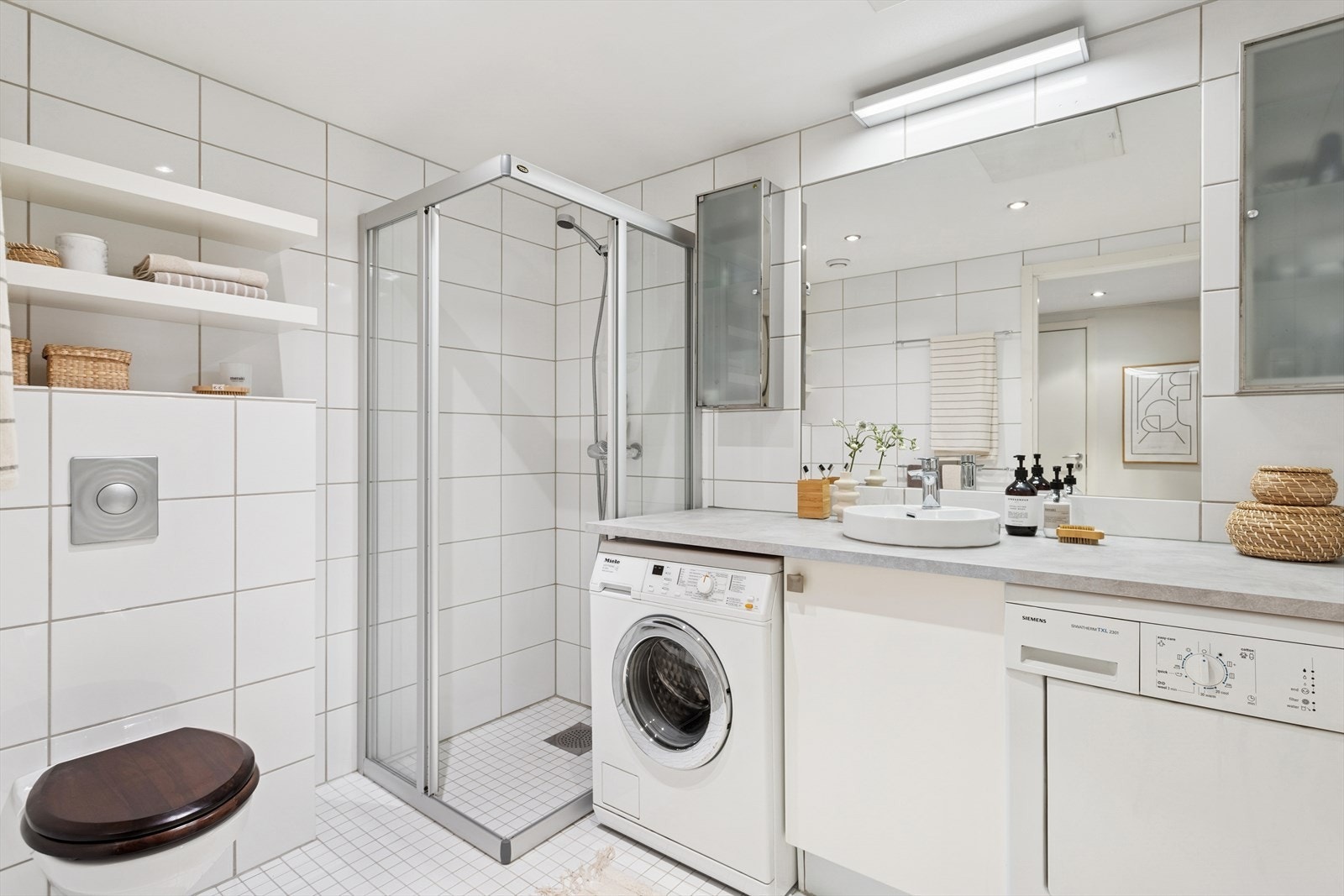 Stort baderom hvor fallforholdet har fått TG1 av takstmann. Innredningen består av servant fra 2020, vegghengt toalett og dusjvegger/hjørne, samt opplegg for vaskemaskin og tørketrommel. For å bidra til behagelig varme er det varmekabler på badet. Galleribilde