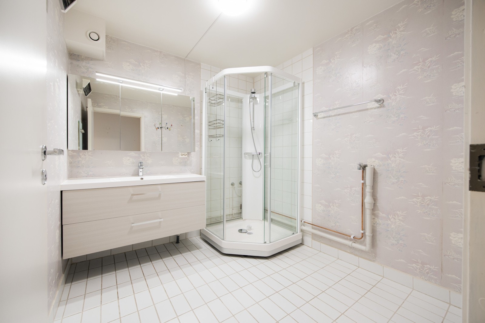 Badet er innredet med servantinnredning, speil i dører på overskap på vegg over servant, dusjkabinett og opplegg for vaskemaskin. Galleribilde