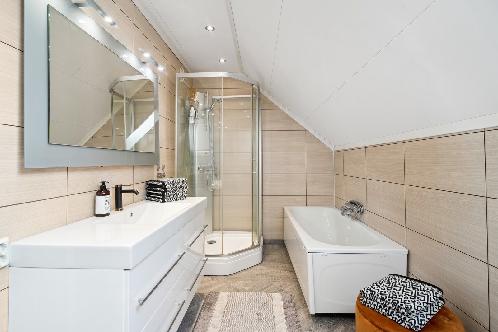 Innredet med servantinnredning, speil med belysning over, vegghengt toalett, badekar og dusjkabinett. Galleribilde