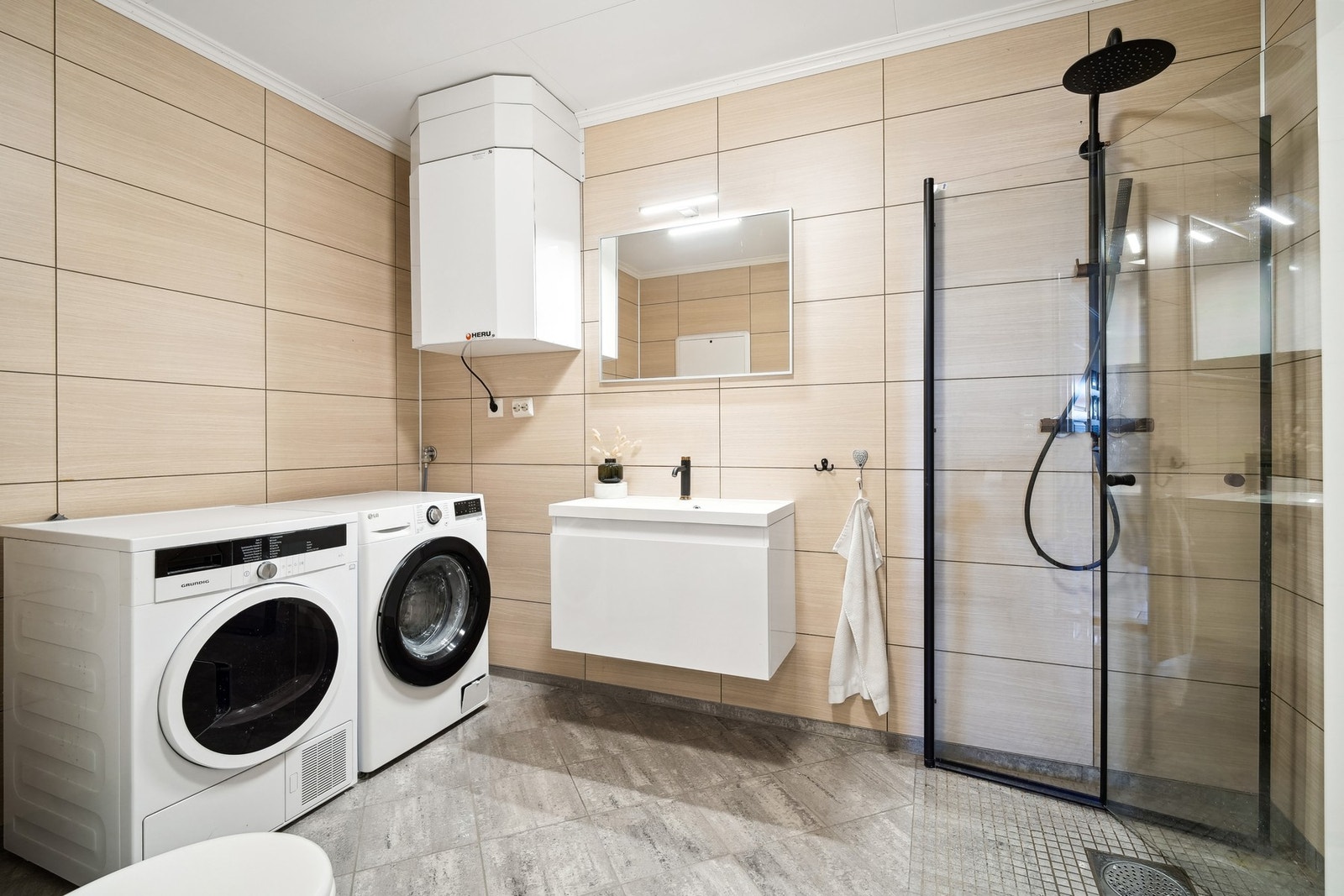 Innredet med vegghengt toalett, servantinnredning, speil med belysning over, dusjhjørne, opplegg for vaskemaskin og tørketrommel. Galleribilde