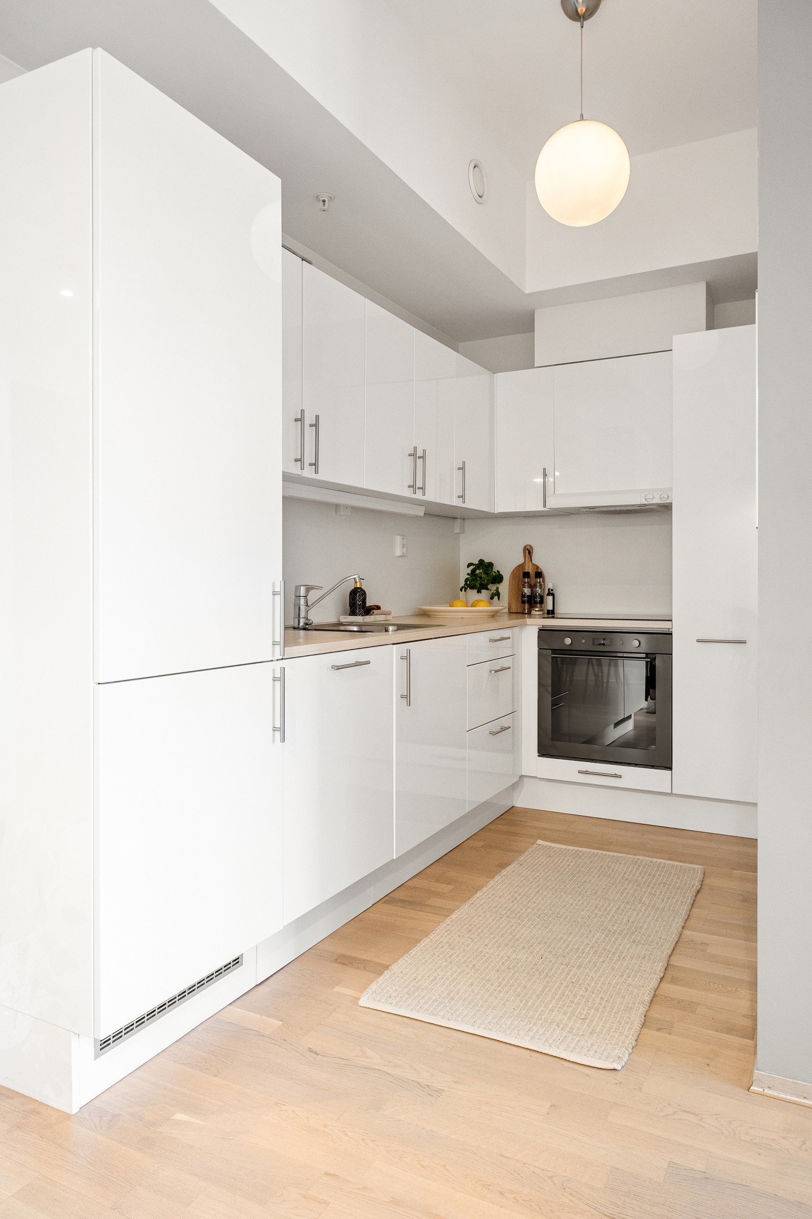 Kjøkkeninnredning fra Aubo med hvite slette høyglans fronter, stålhåndtak og overskap med benkebelysning Galleribilde