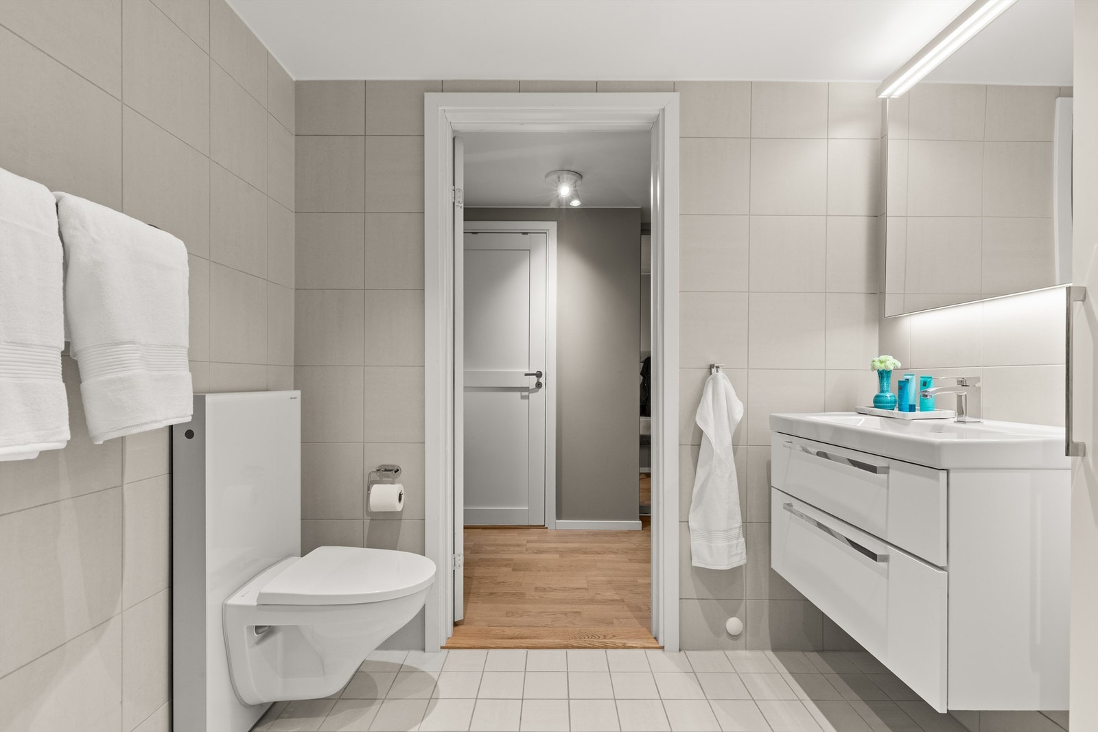 Stilrent og pent flislagt bad med varmekabler i gulv. Badet er innredet med vegghengt klosett, servant nedfelt i innredning og speil med belysning. Galleribilde