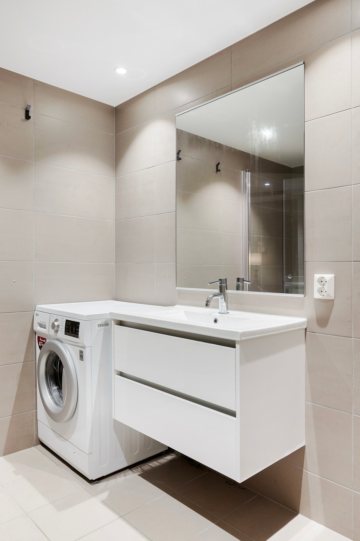 Badet er innredet med dusjhjørne med innfellbare glassdører, servantskap, vegghengt toalett, speil og opplegg for vaskemaskin. Galleribilde