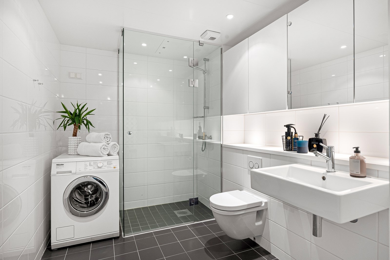 Delikat flislagt baderom med gulvvarme og downlights i himlingen. Badet har en stilren servant, veggskap med to speildører og et vegghengt klosett med innebygd sisterne. Galleribilde