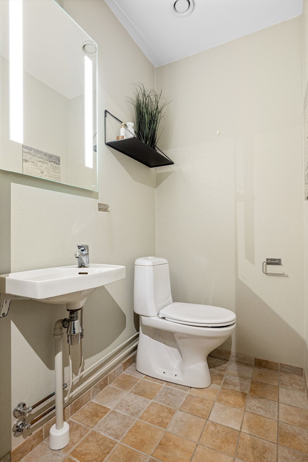 Separat toalettrom med flislagt gulv og malte veggflater. Rommet er innredet med toalett, servant og speil med belysning Galleribilde