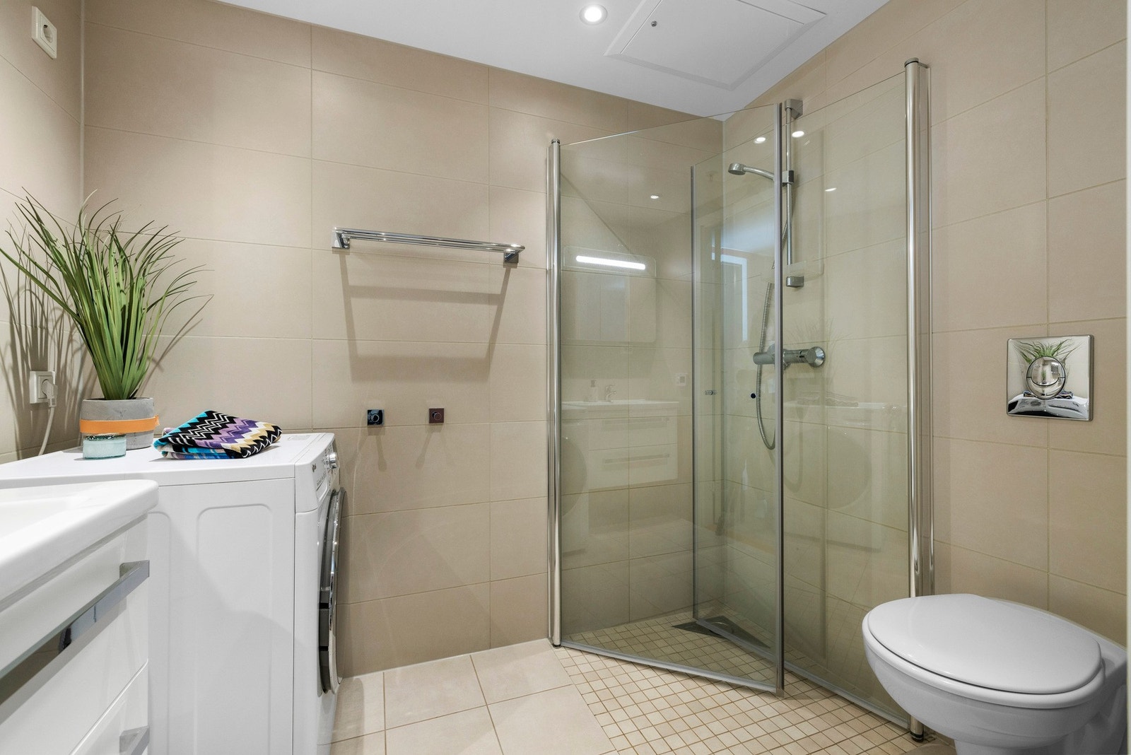 Det er varmekabler i gulvet og innredningen består av nedfelt servant med to praktiske skuffer for ekstra oppbevaring, speilskap over servant med integrert lys og stikkontakt, vegghengt toalett, plassbesparende innfellbare dusjdører samt opplegg for vaske Galleribilde