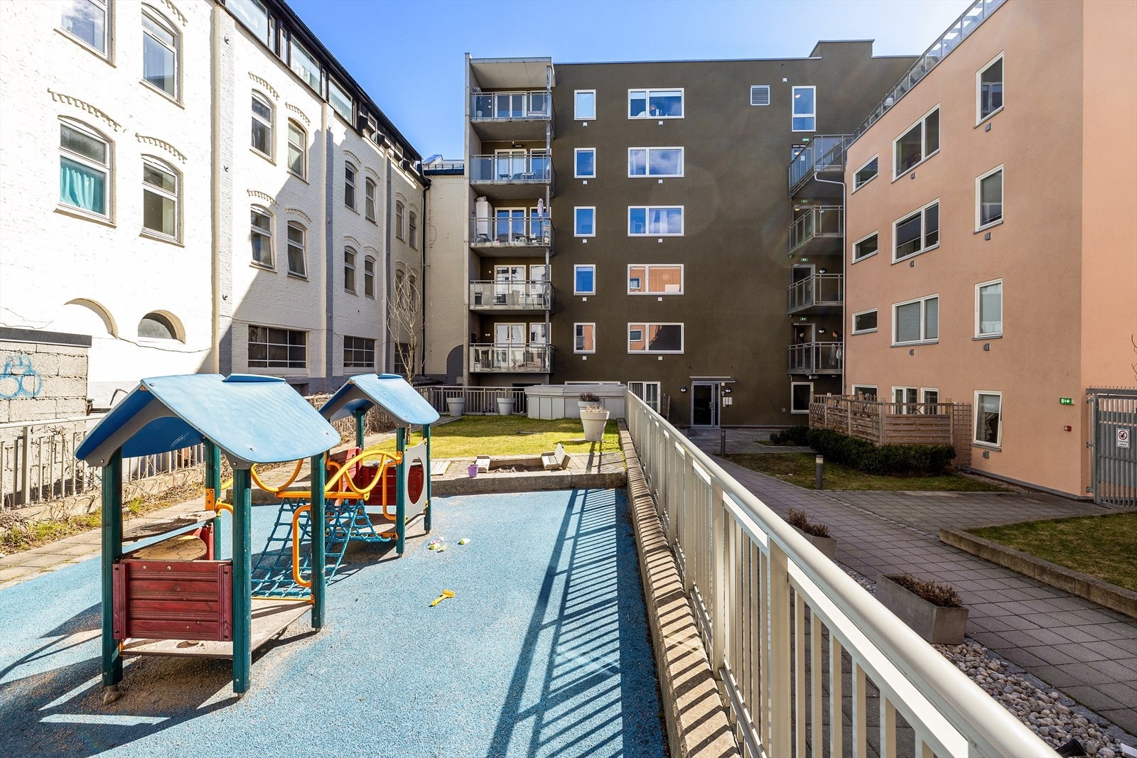 Opparbeidet gårdsrom med noe gressplen, lekeplass, betongheller, utebelysning og beplantning. Galleribilde