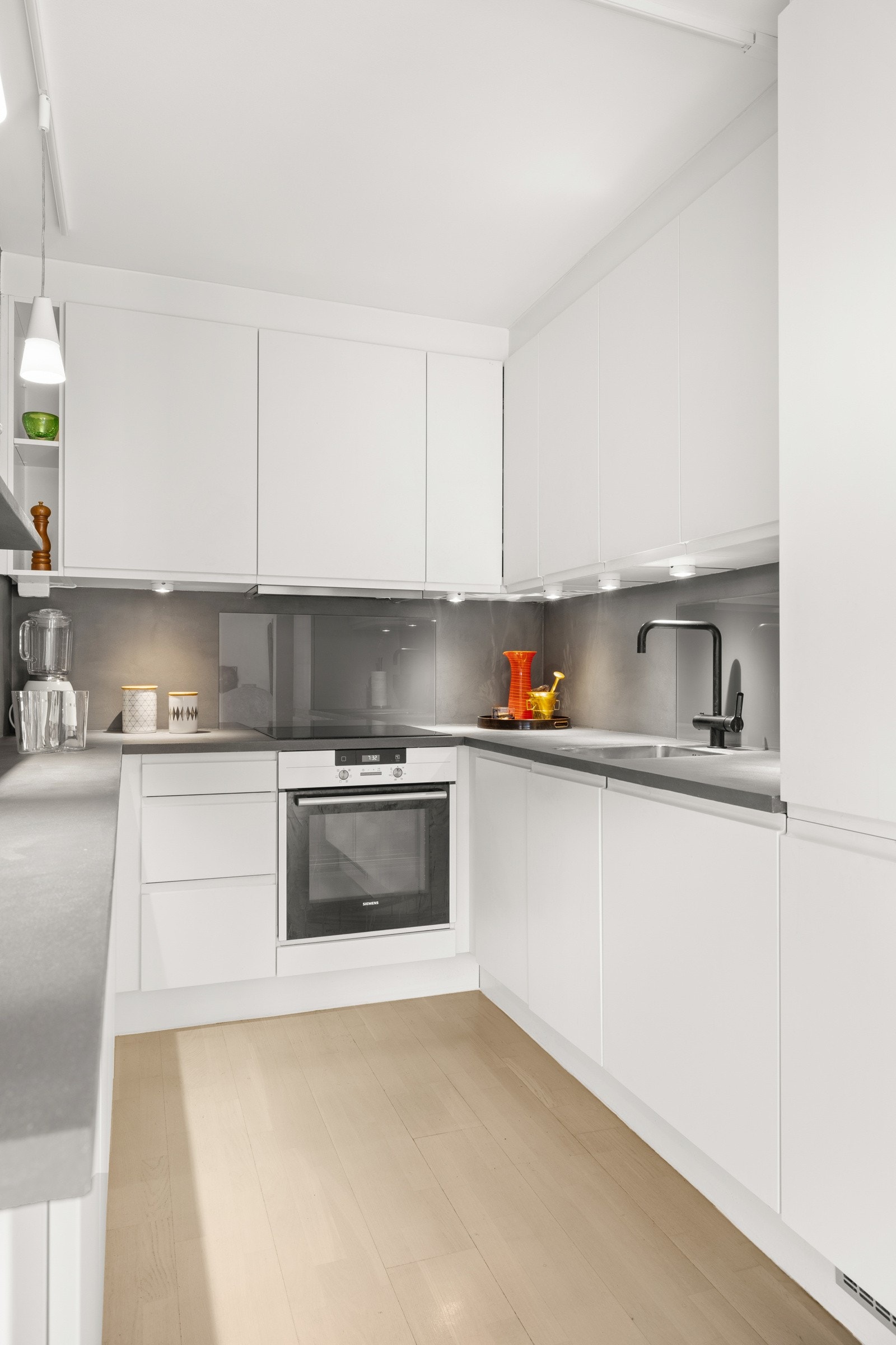 Malt flate og glassplater mellom benkeplate og overskap samt benkeskapsbelysning og stikkontakter under overskap. Galleribilde