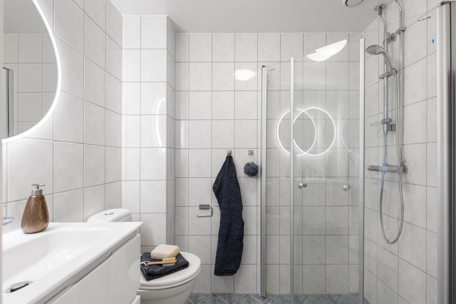 Badet inneholder servant med underskap, speil med integrert belysning, dusjhjørne med svingbare glassdører og frittstående toalett. Galleribilde