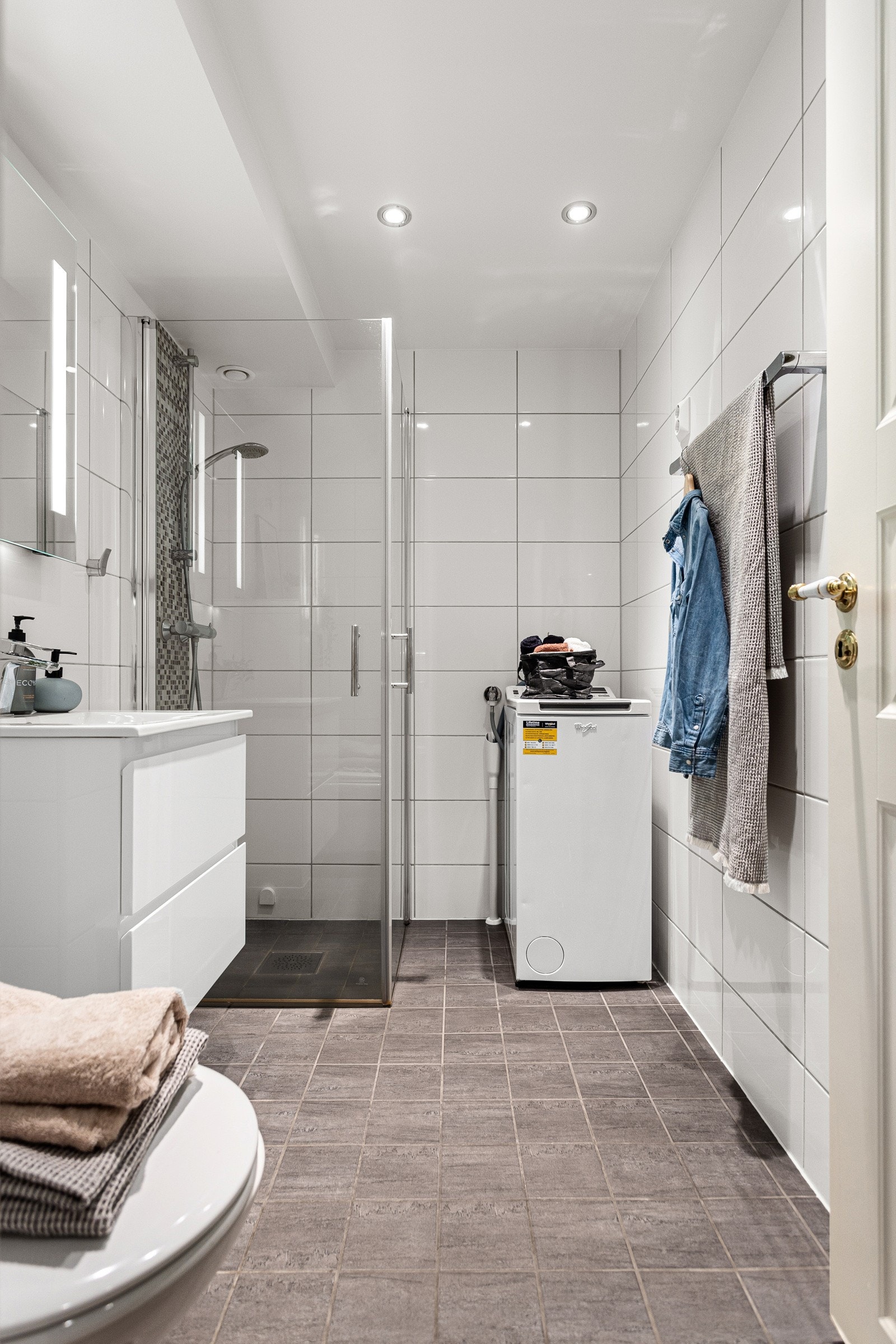 Badet er lyst og moderne med flislagte vegger og gulv, samt opplegg for vaskemaskin og servant med slette fronter Galleribilde