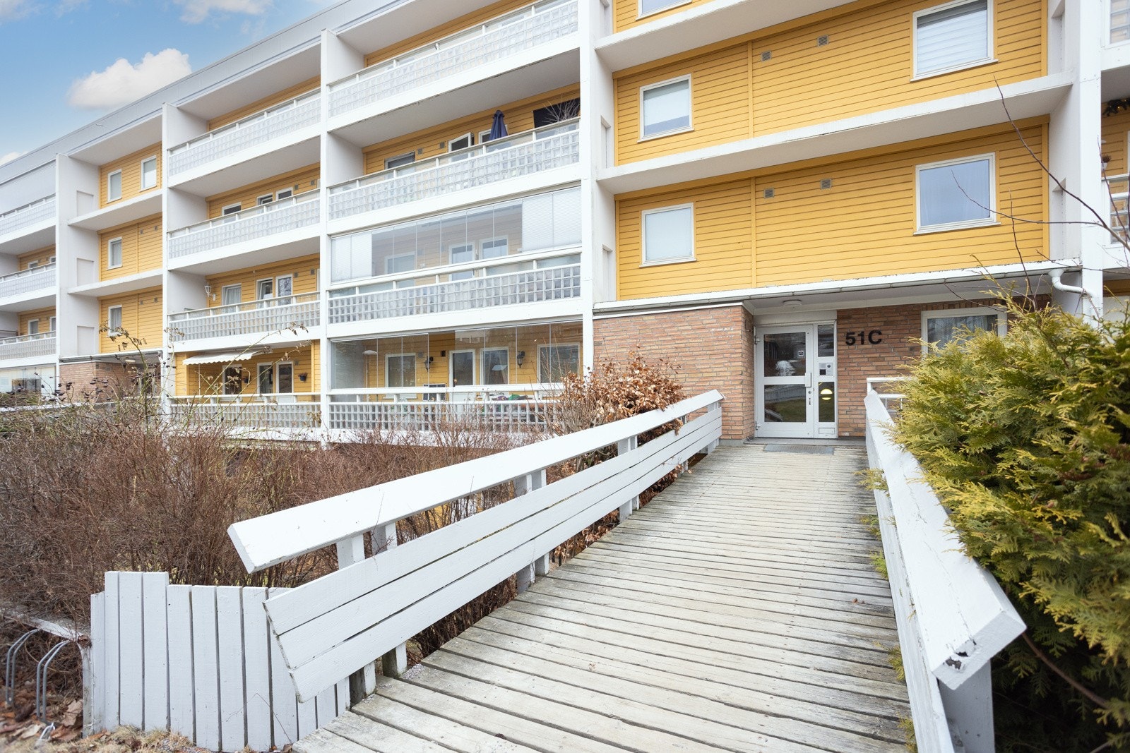 Inngangspartiet inn til felles trappeoppgang er forbundet med en bred gangbro, hvor området rundt er pent beplantet Galleribilde