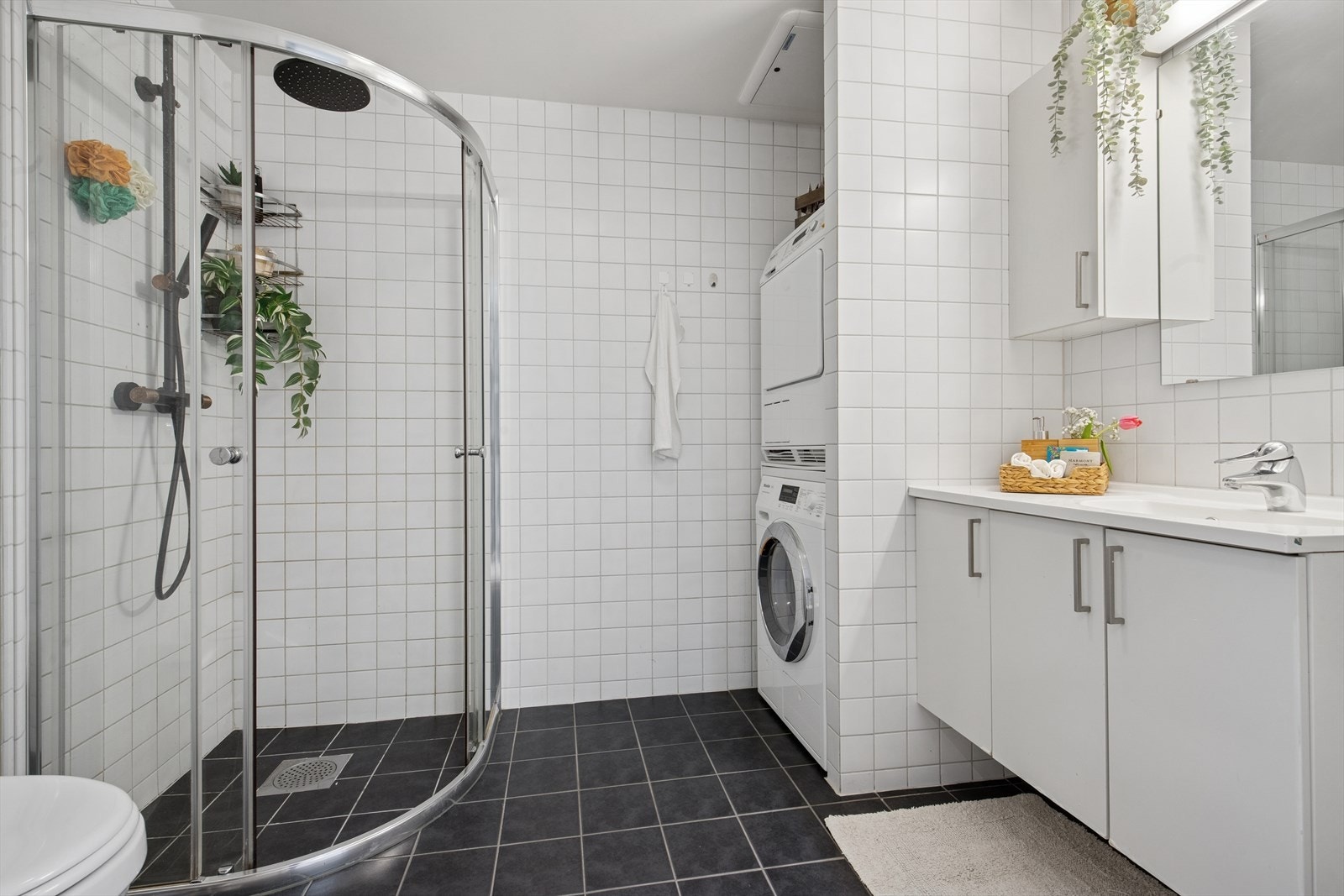 Det helflisede badet har varmekabler i gulvet som gir behagelig oppvarming. Badet har innredning med nedfelt servant, et dusjhjørne med elegante glassvegger og dusjkant, et vegghengt toalett, og opplegg for vaskemaskin. Galleribilde