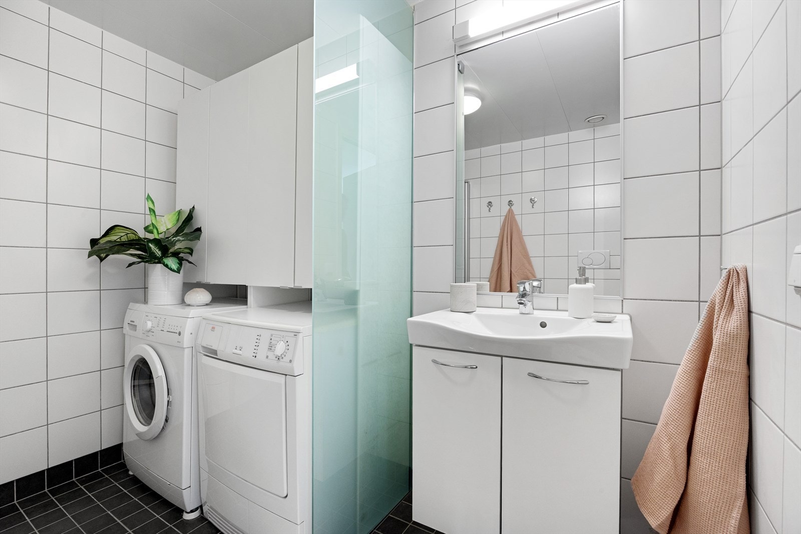 Baderommet er funksjonelt innredet med vegghengt toalett, dusj med elegante glass foldedører, servant med moderne møblement, speil og belysning. Galleribilde