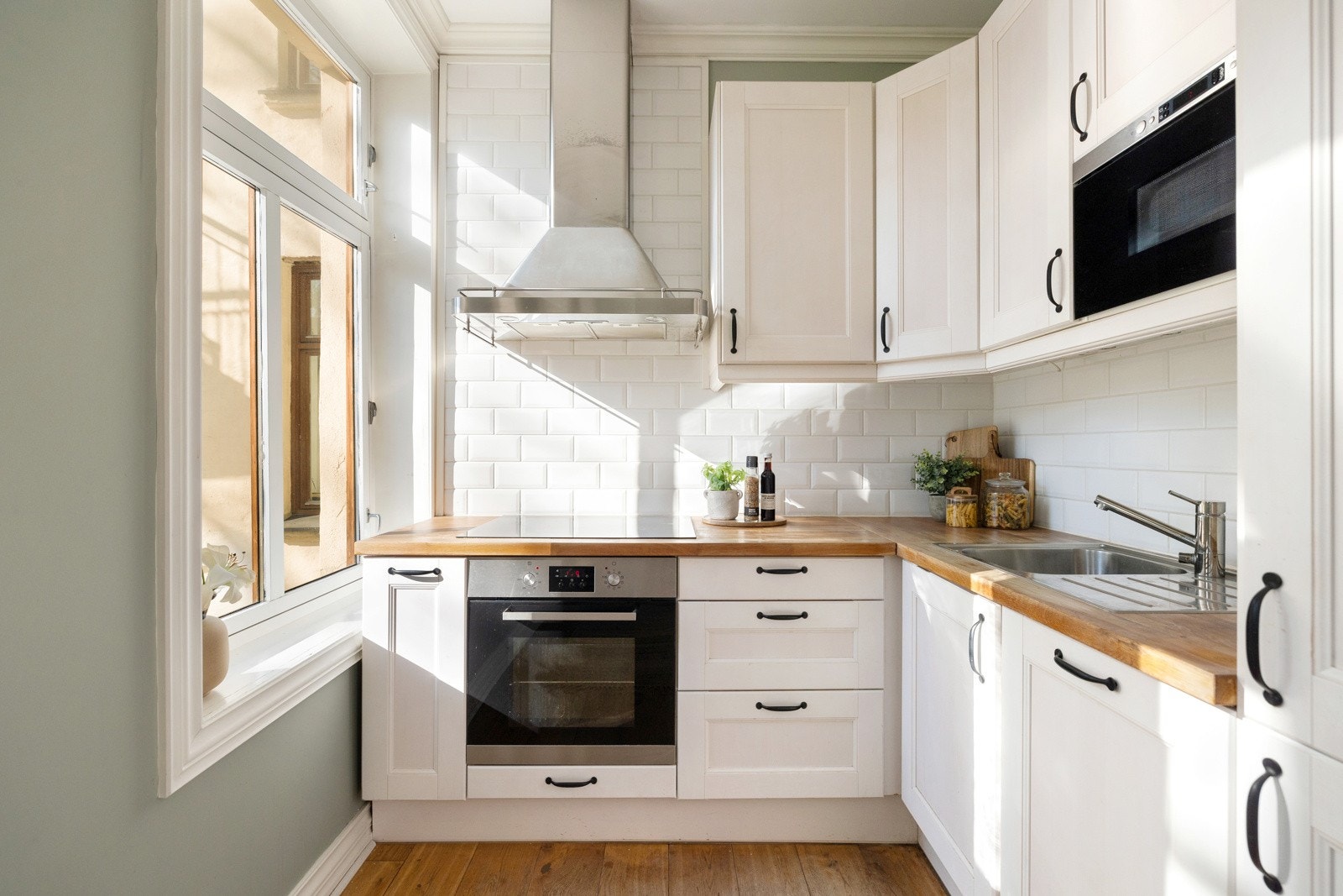 Kjøkkeninnredning har profilerte hvite fronter, fliser mellom overskap og benk, og benkeplate av tre med nedfelt kum i stål Galleribilde