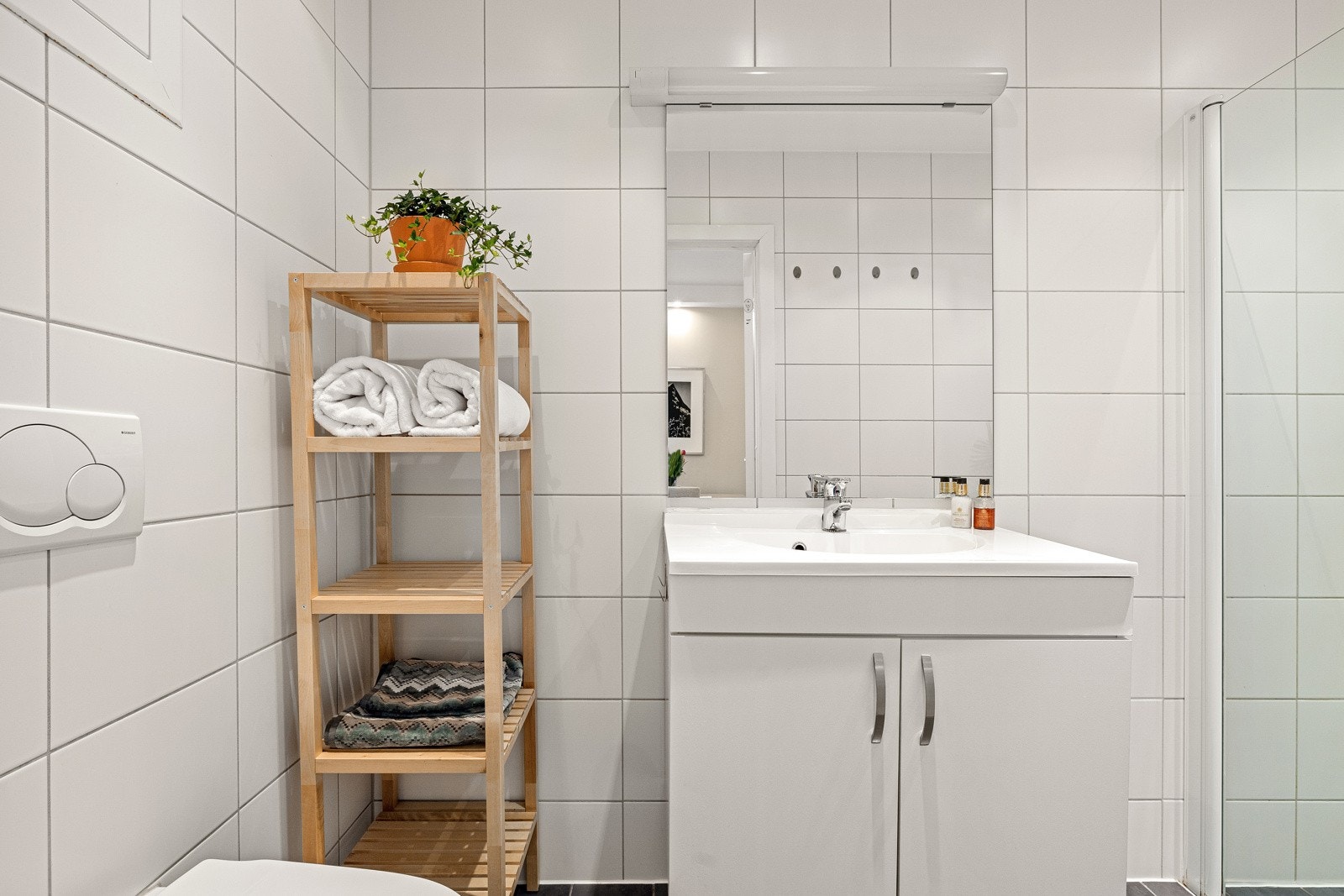 Baderommet har grå fliser på gulv med gulvvarme, hvite fliser på veggene, downlights i himlingen og avtrekksventiler i vegg. Galleribilde