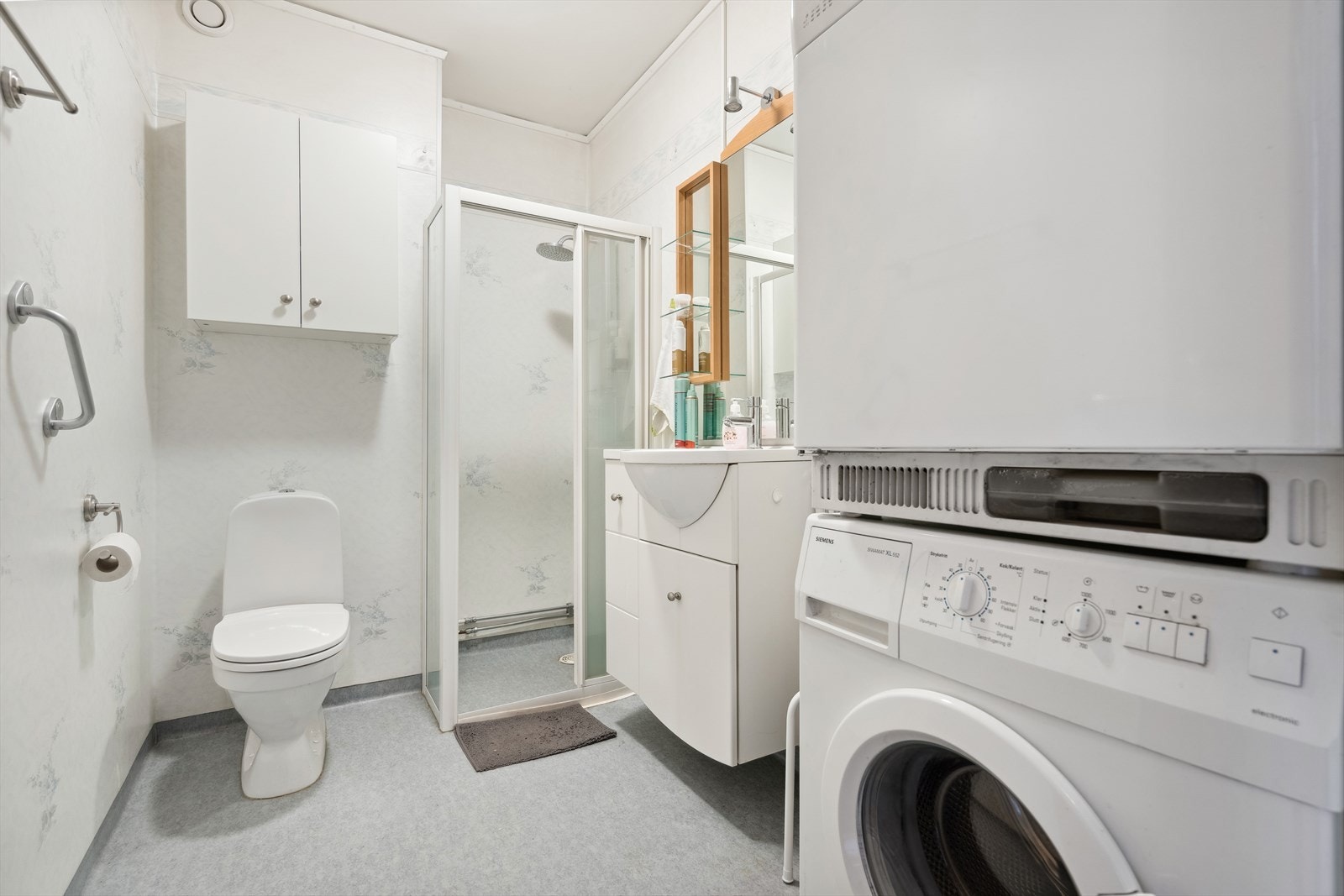 Innredet med dusjhjørne, gulvmontert toalett, baderomsinnredning med speil og lys, opplegg for vaskemaskin og tørketrommel. Galleribilde