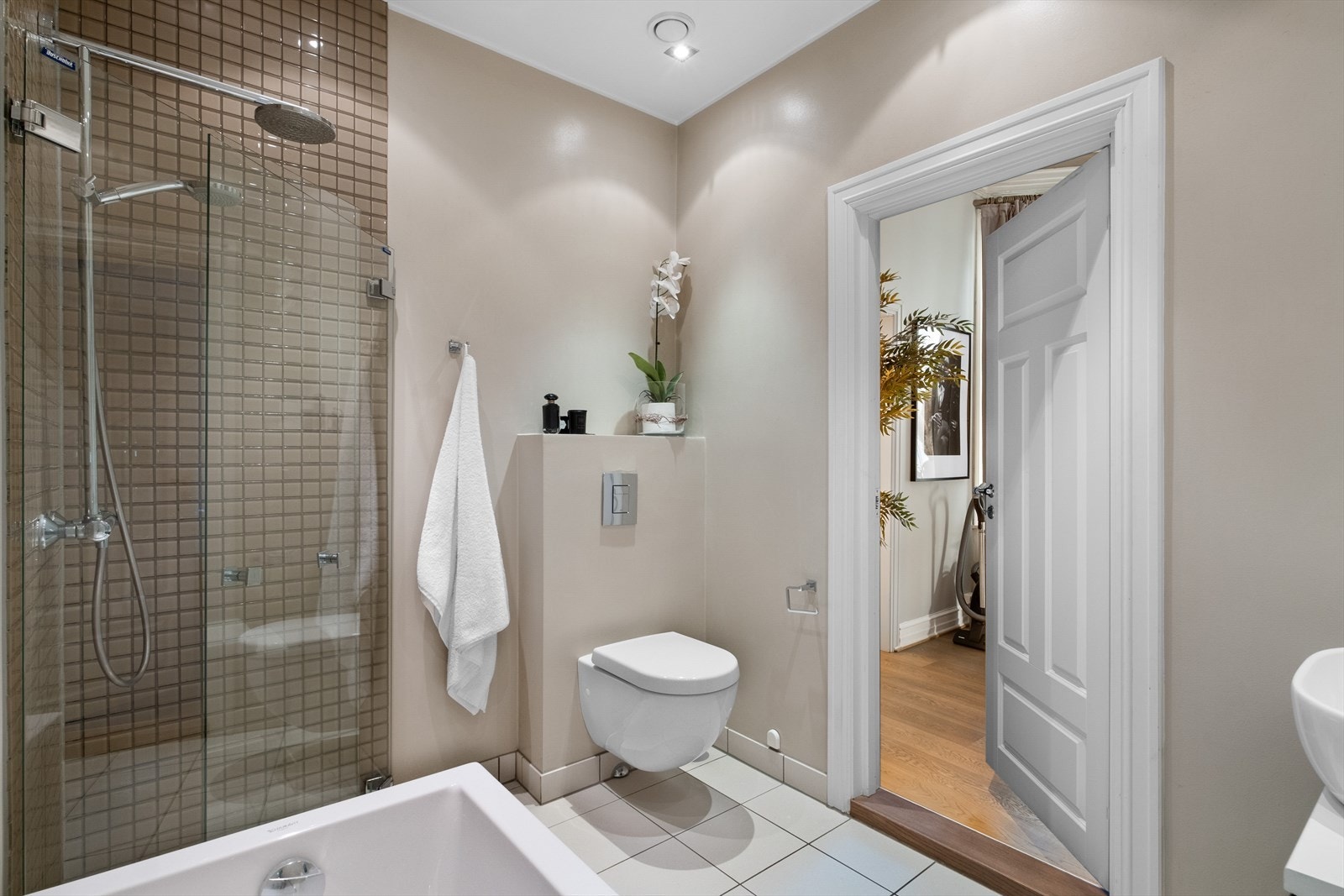 Baderommet er innredet med vegghengt klosett, servant plassert på innredning, innfelt speil, badekar og dusjhjørne med svingbare glassdører. Mekanisk avtrekk. Galleribilde