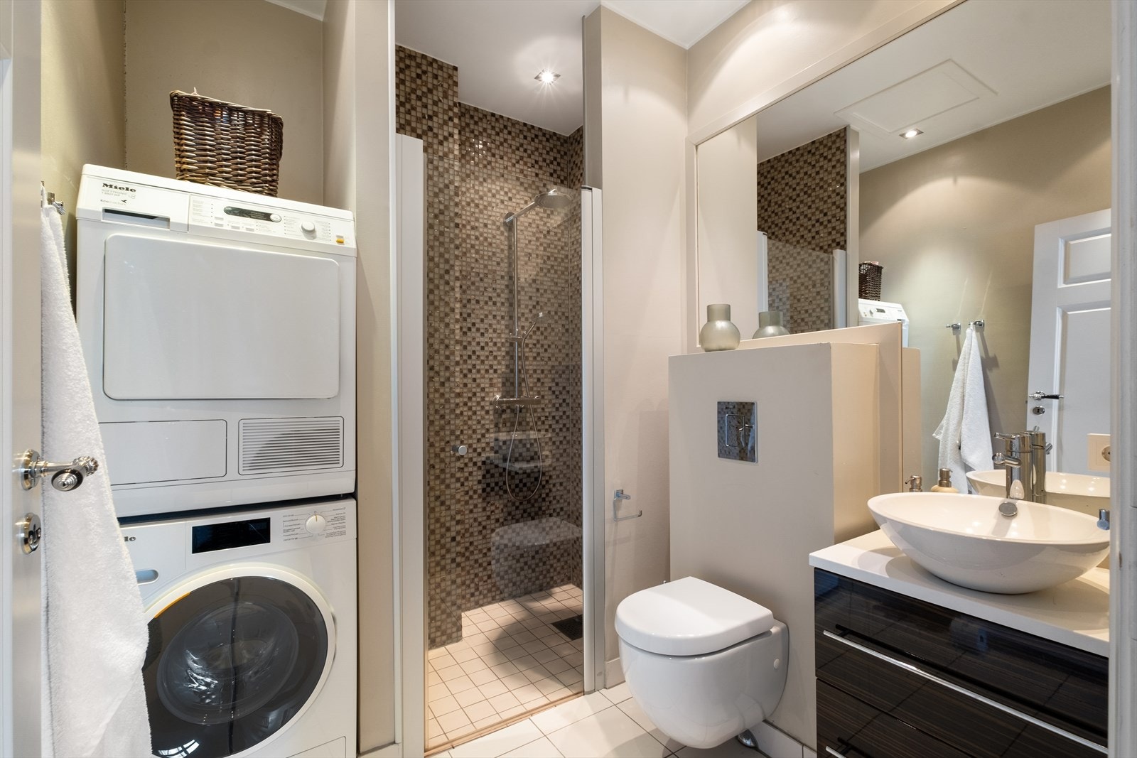 Ved TV-stuen er det flislagt bad fra 2012 med varme i gulvet og downlights i himling. Badet er innredet med vegghengt klosett, servant plassert på innredning, innfelt speil og dusjhjørne med svingbar glassdør. Opplegg for vask/tørk. Mekanisk avtrekk. Galleribilde