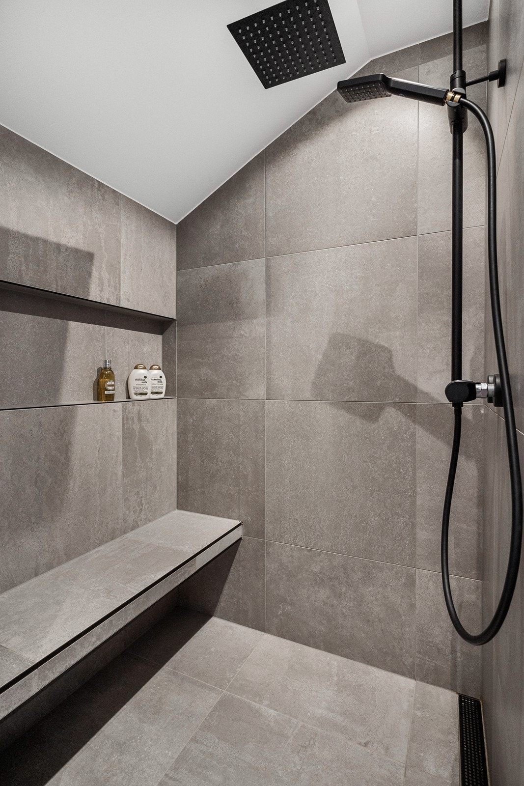 Videre har badet en stor dusjnisje med flislagt benk, slukrenne og sorte detaljer. Galleribilde
